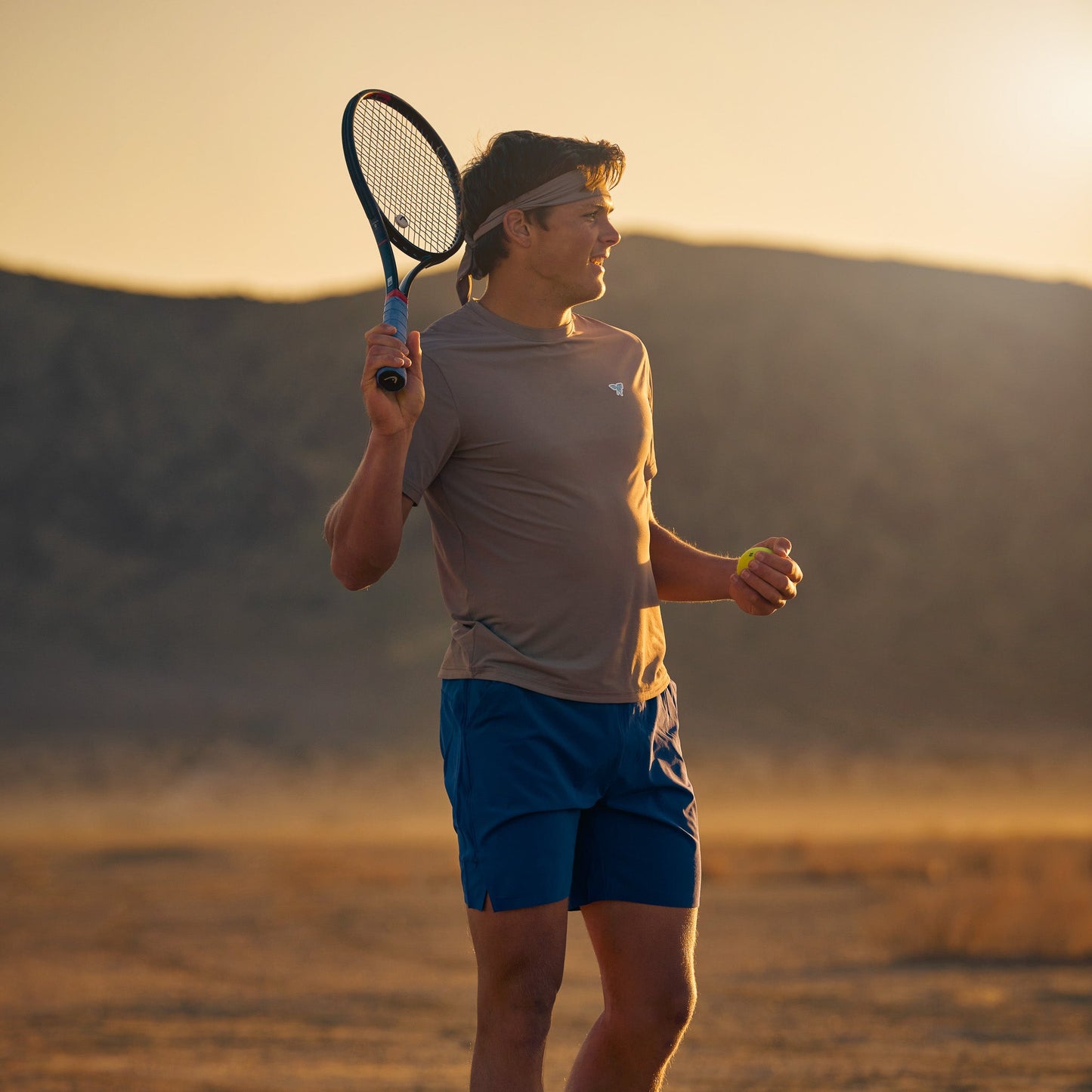 Model wearing Sigrún match tee in gray in playing tennis in a desert.