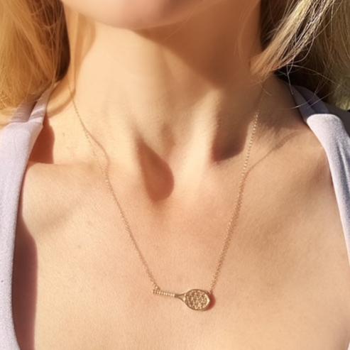 amelia rose Gold necklace with a tennis racket pendant on a person wearing a white shirt.