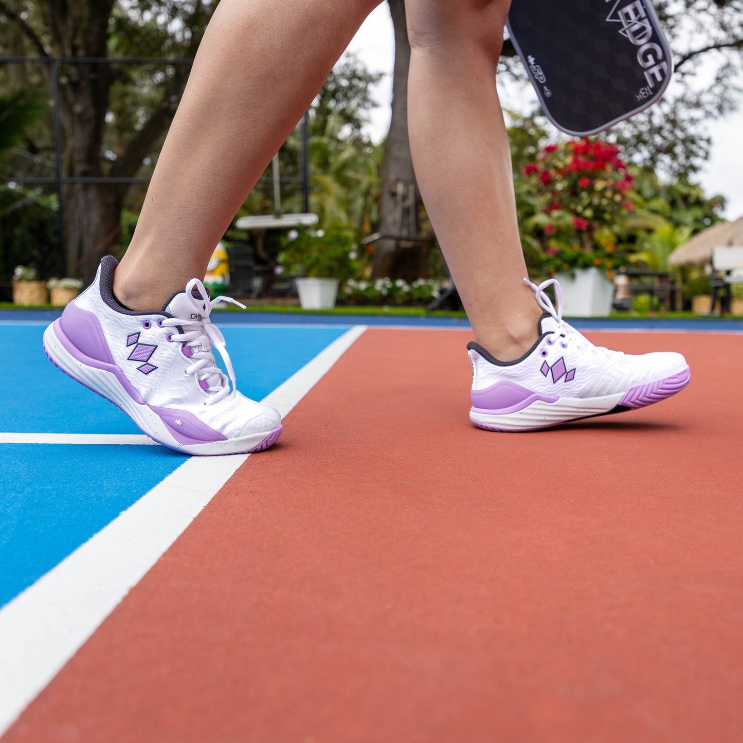 Person wearing white and purple athletic shoes on a tennis court