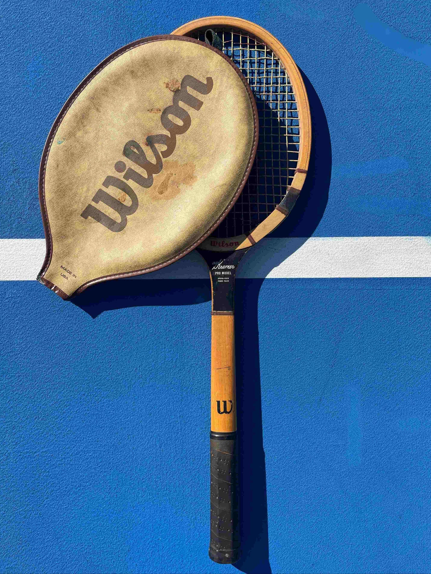 Vintage Jack Kramer Wooden Tennis Racquet on blue tennis court with white line.