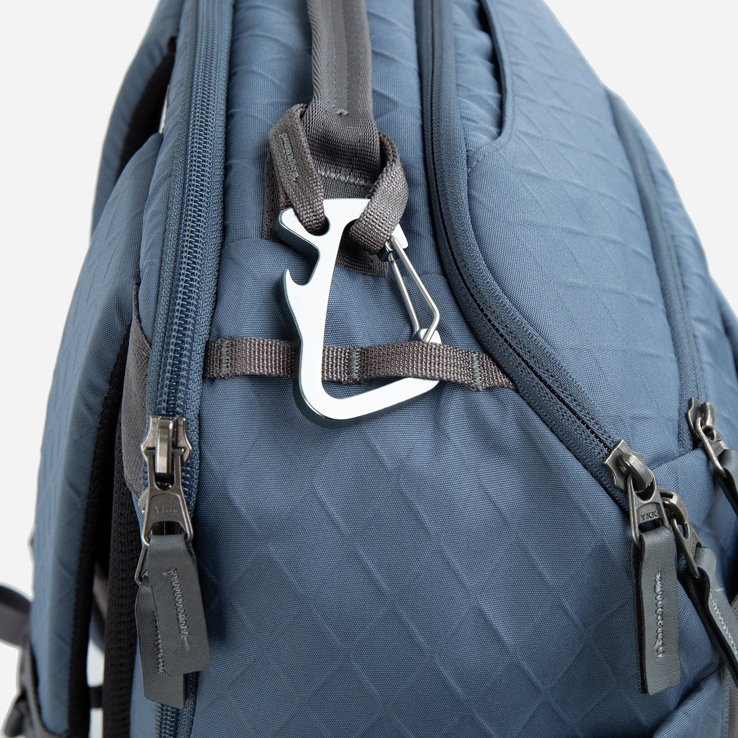 Close-up of a blue Doubletake tennis backpack with zippers and a carabiner on a white background
