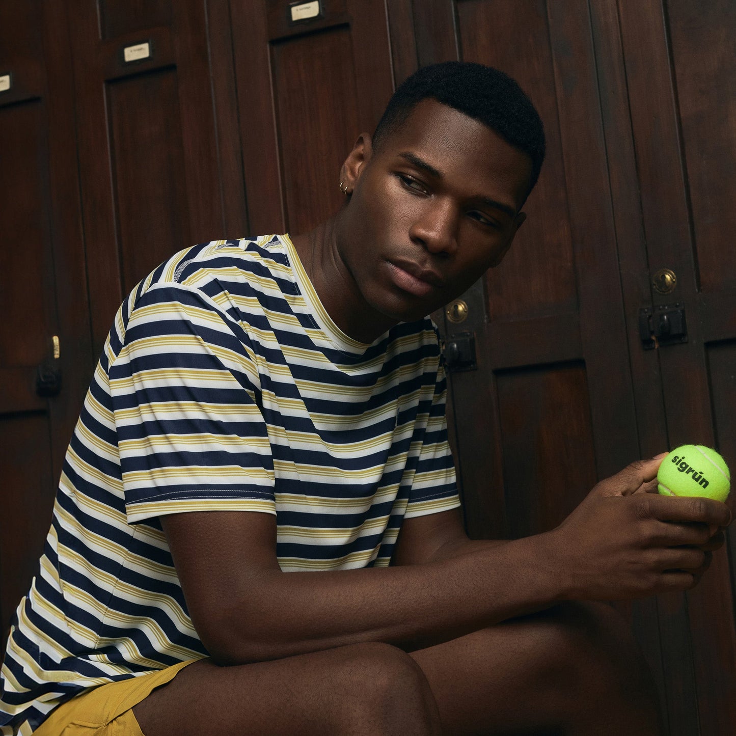 Black model wearing striped Sigrún match tee holding a tennis ball.