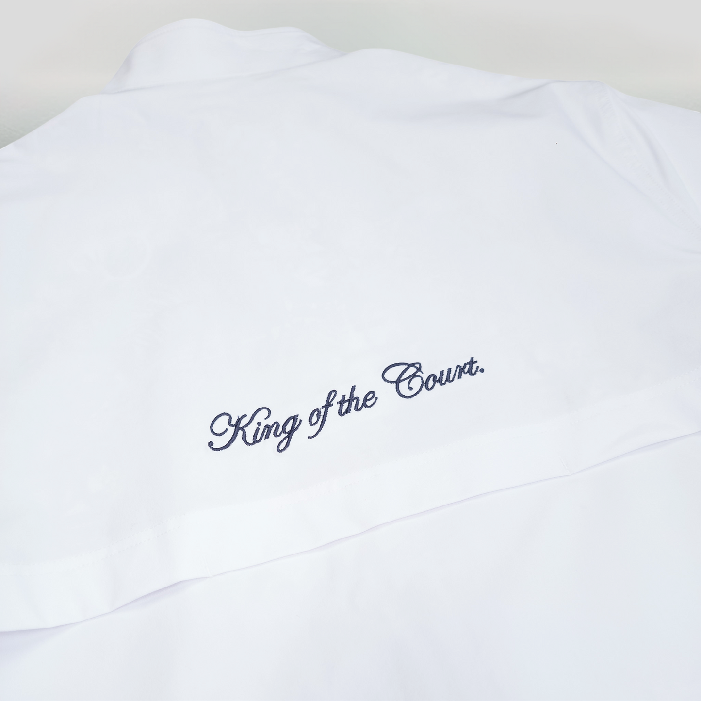 Sigrún match jacket in white with close up of "king of the court" written on the back in navy.