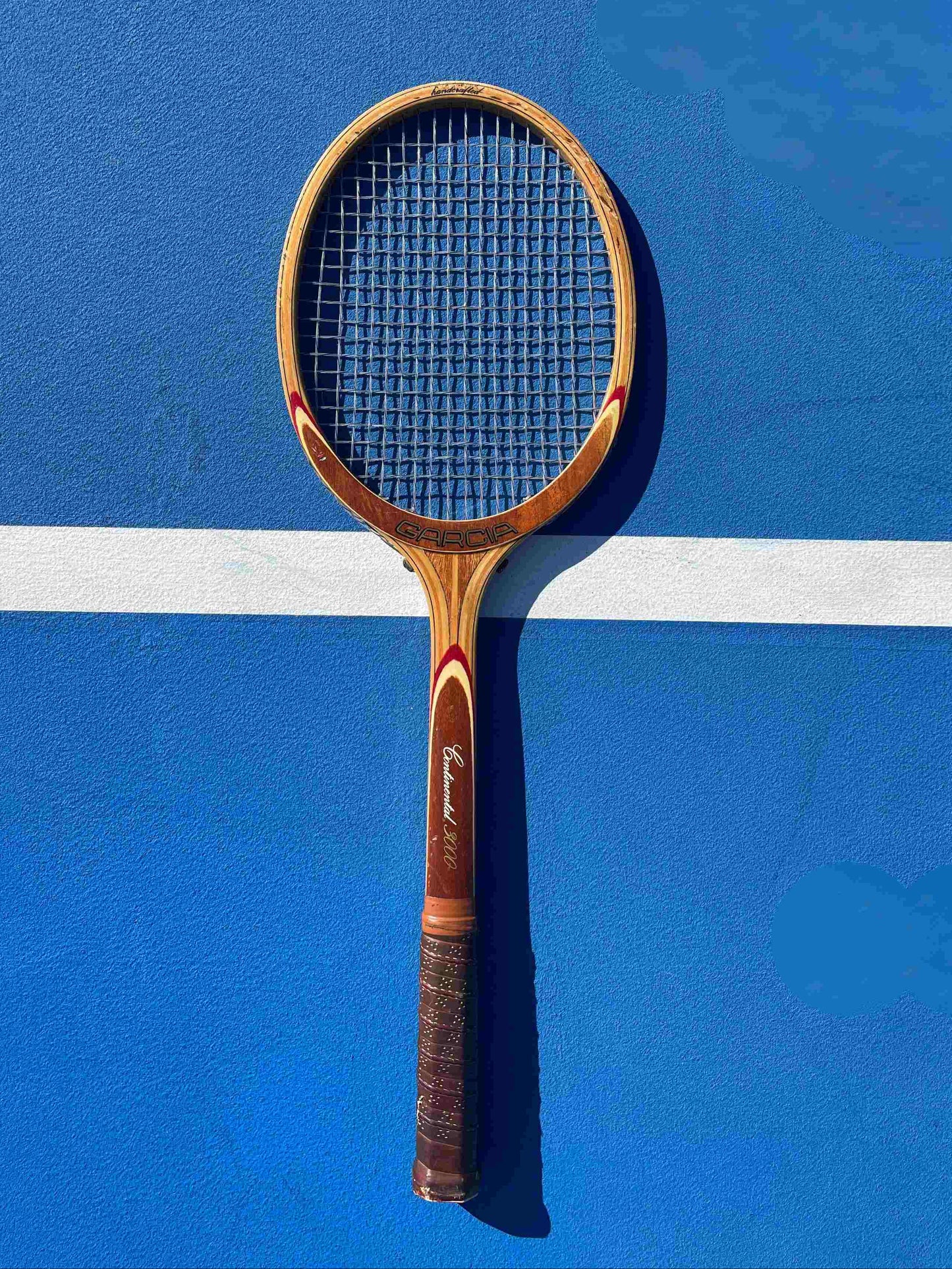 Garcia Continental Wood Tennis Racquet on blue court with white line. 