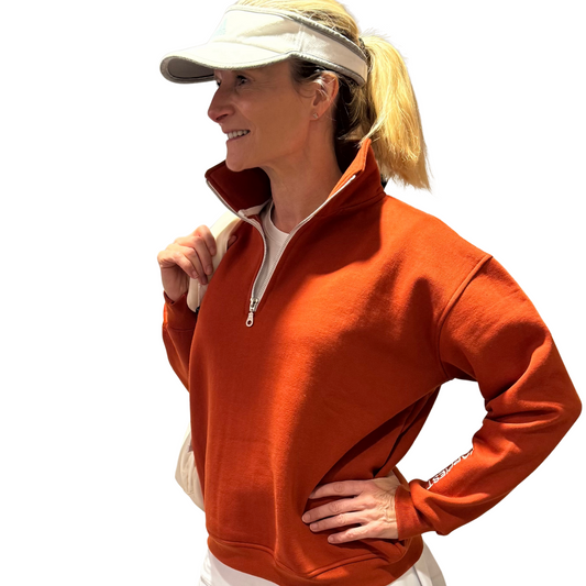 Woman wearing an orange half-zip sweatshirt and white visor on a white background