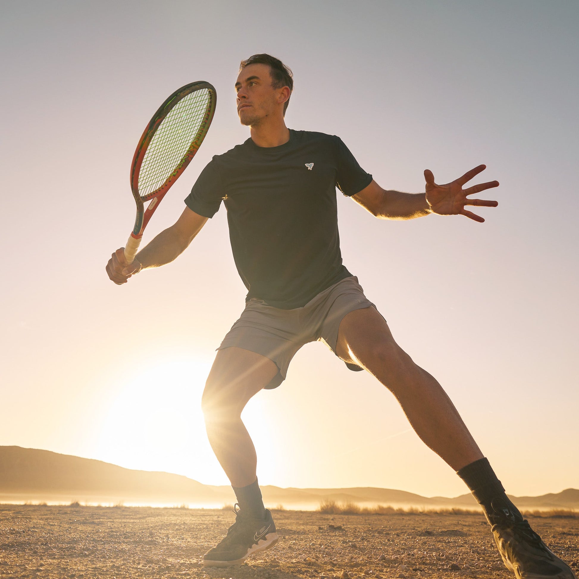 Male model wearing Sigrún match tee in black holding a tennis racquet. 
