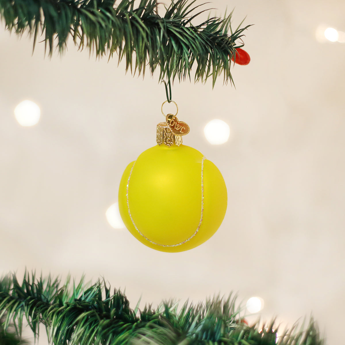Yellow Christmas ornament shaped like a tennis ball hanging on a tree branch.