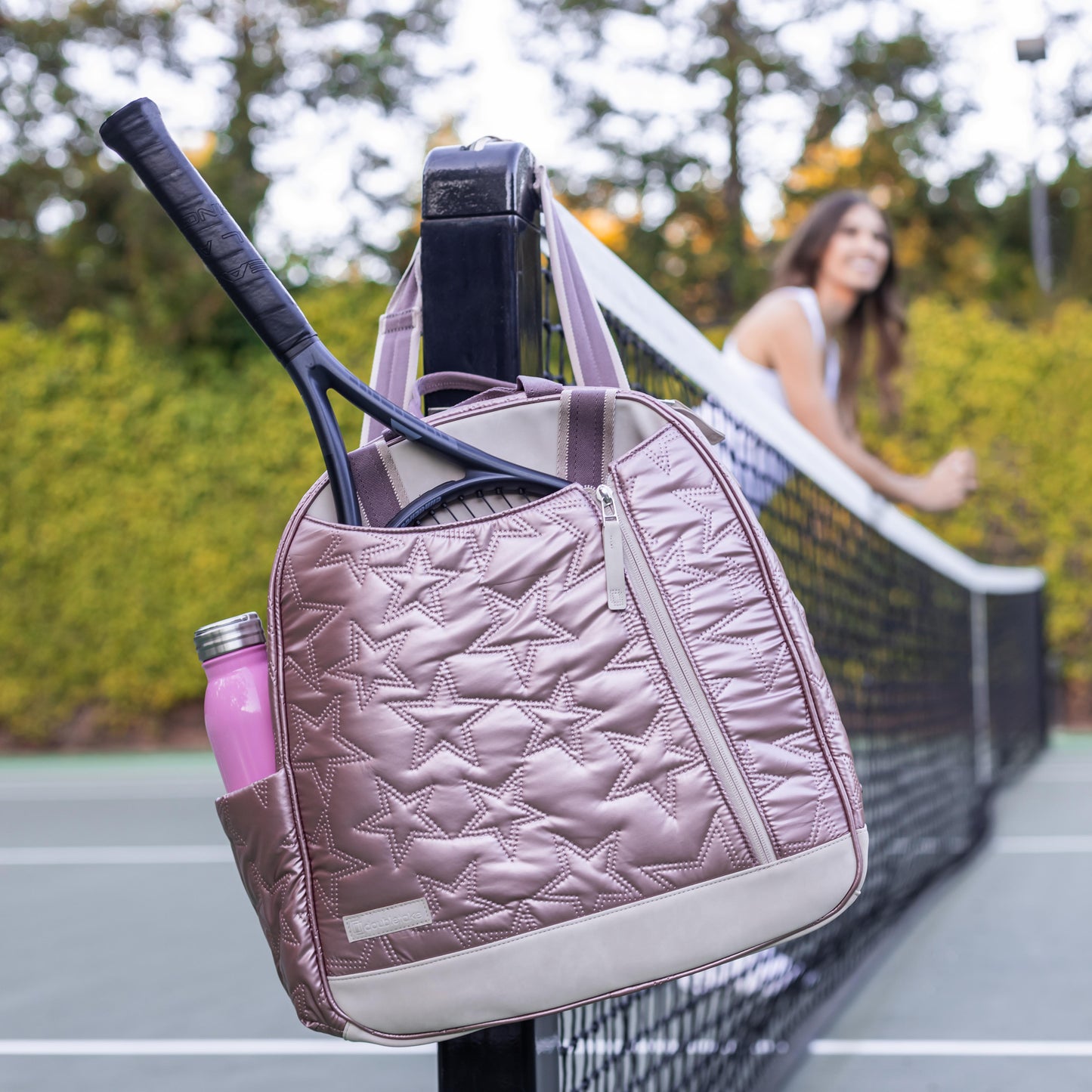 Pink  Doubletake tennis quilted tennis bag with a racket and bottle on a tennis court