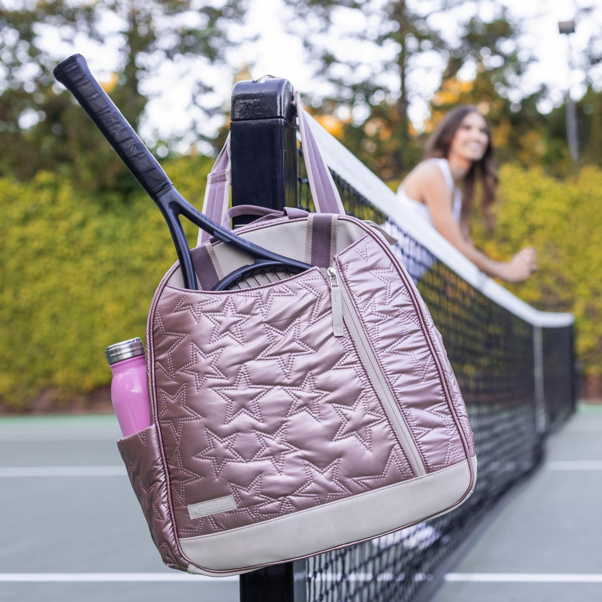 Pink  Doubletake tennis quilted tennis bag with rackets and a bottle on a tennis court
