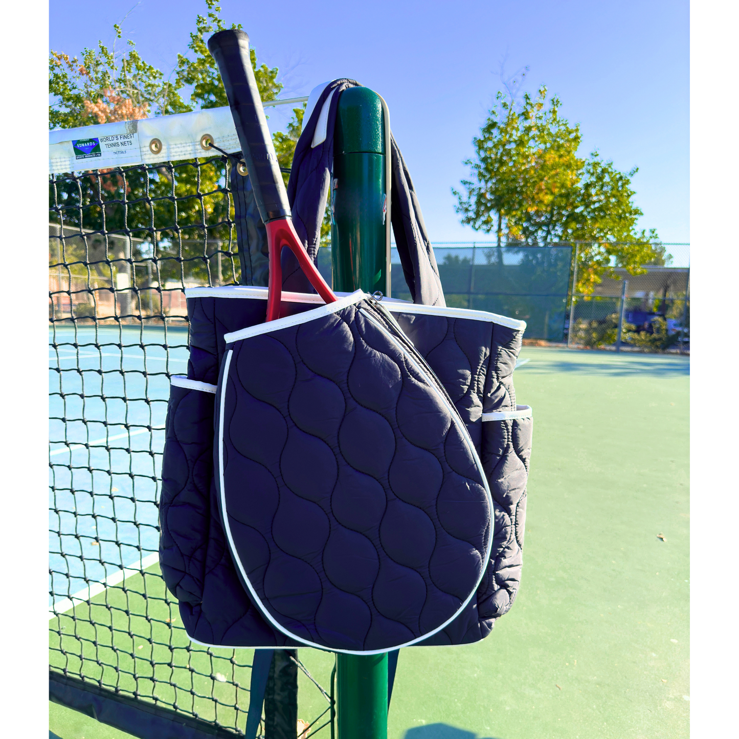 Navy blue quilted tennis bag with a red tennis racket on a tennis court