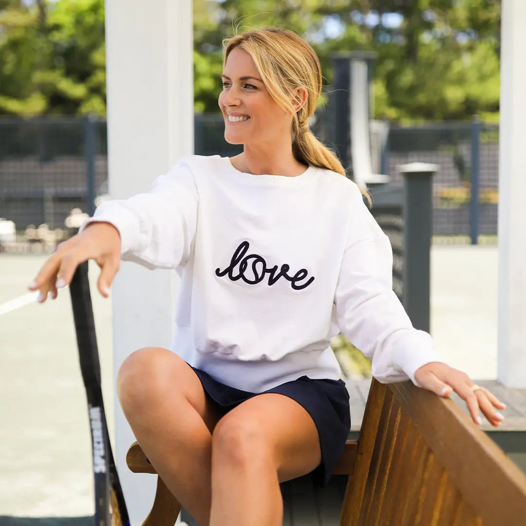 Woman wearing a white sweatshirt with 'love' printed on it, sitting outdoors.