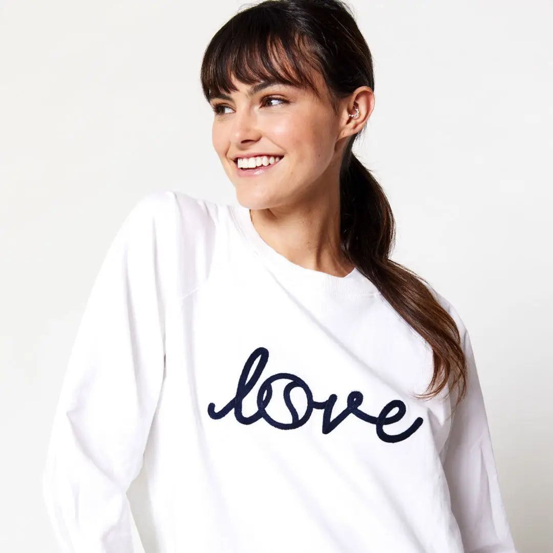 Woman wearing a white tennis sweatshirt with 'love' printed on it against a plain background