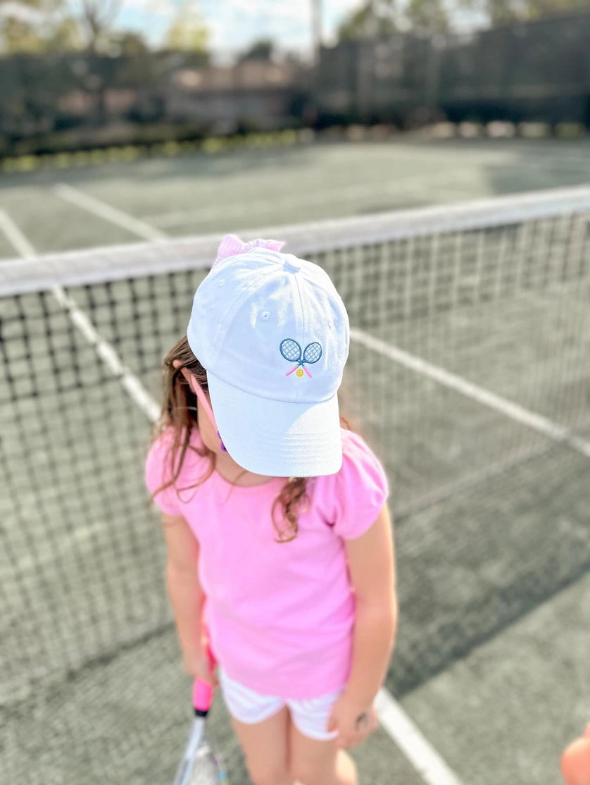 Child wearing white cap with a tennis logoon a tennis court