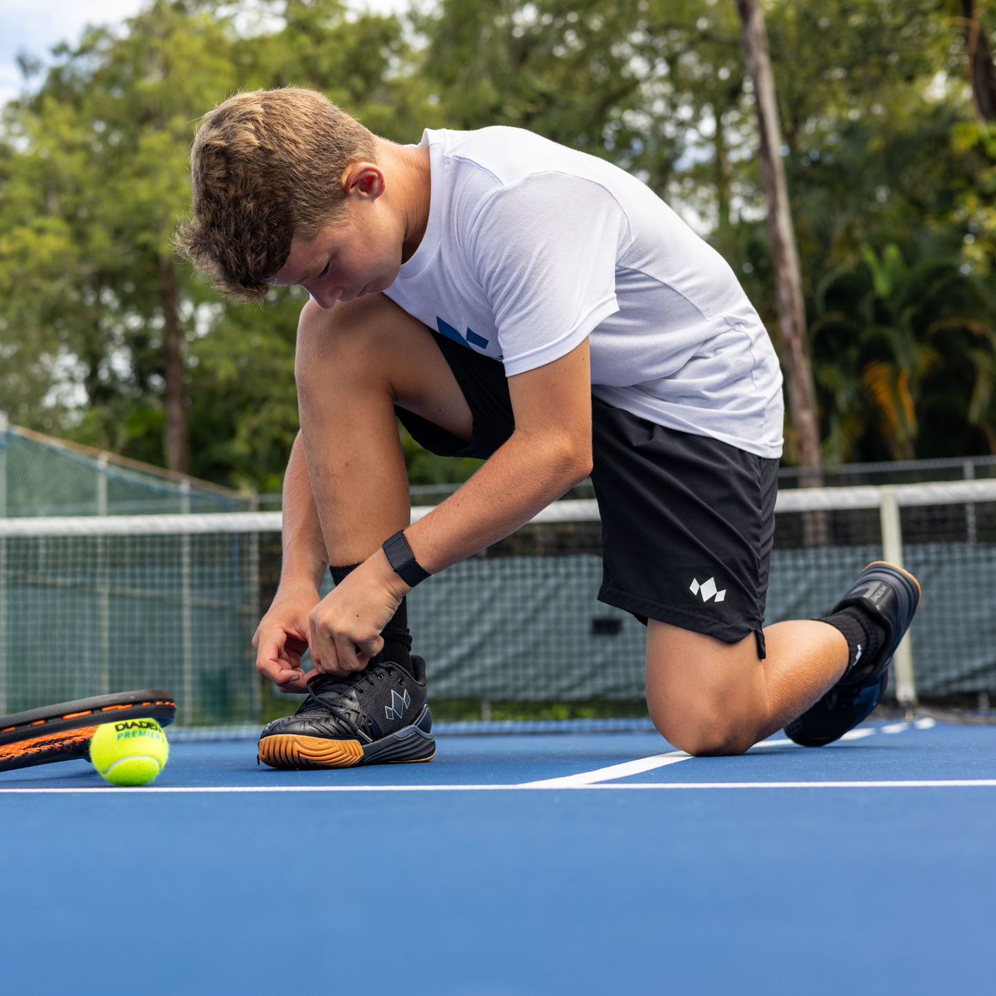 Person tying shoes on a tennis court with a tennis ball nearby