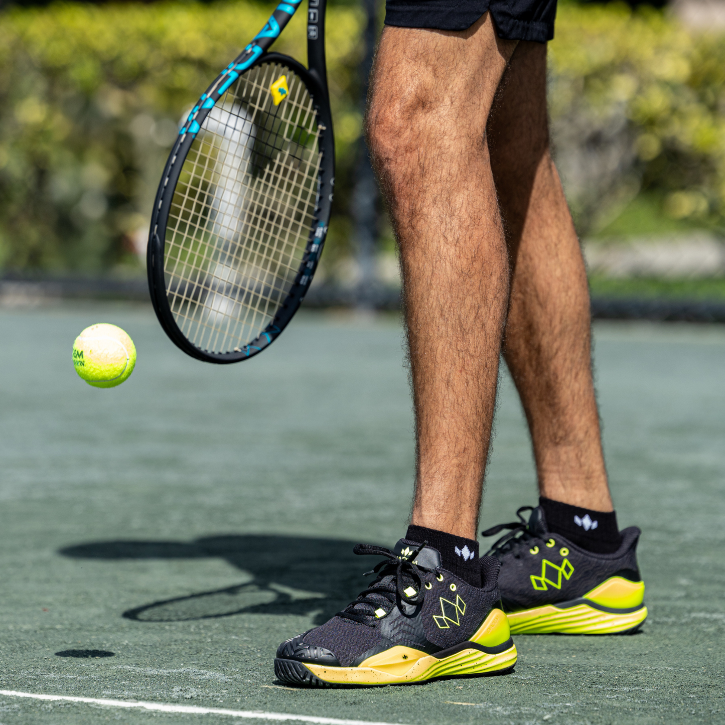 Person on a tennis court with a racket and ball, wearing black and yellow shoes.