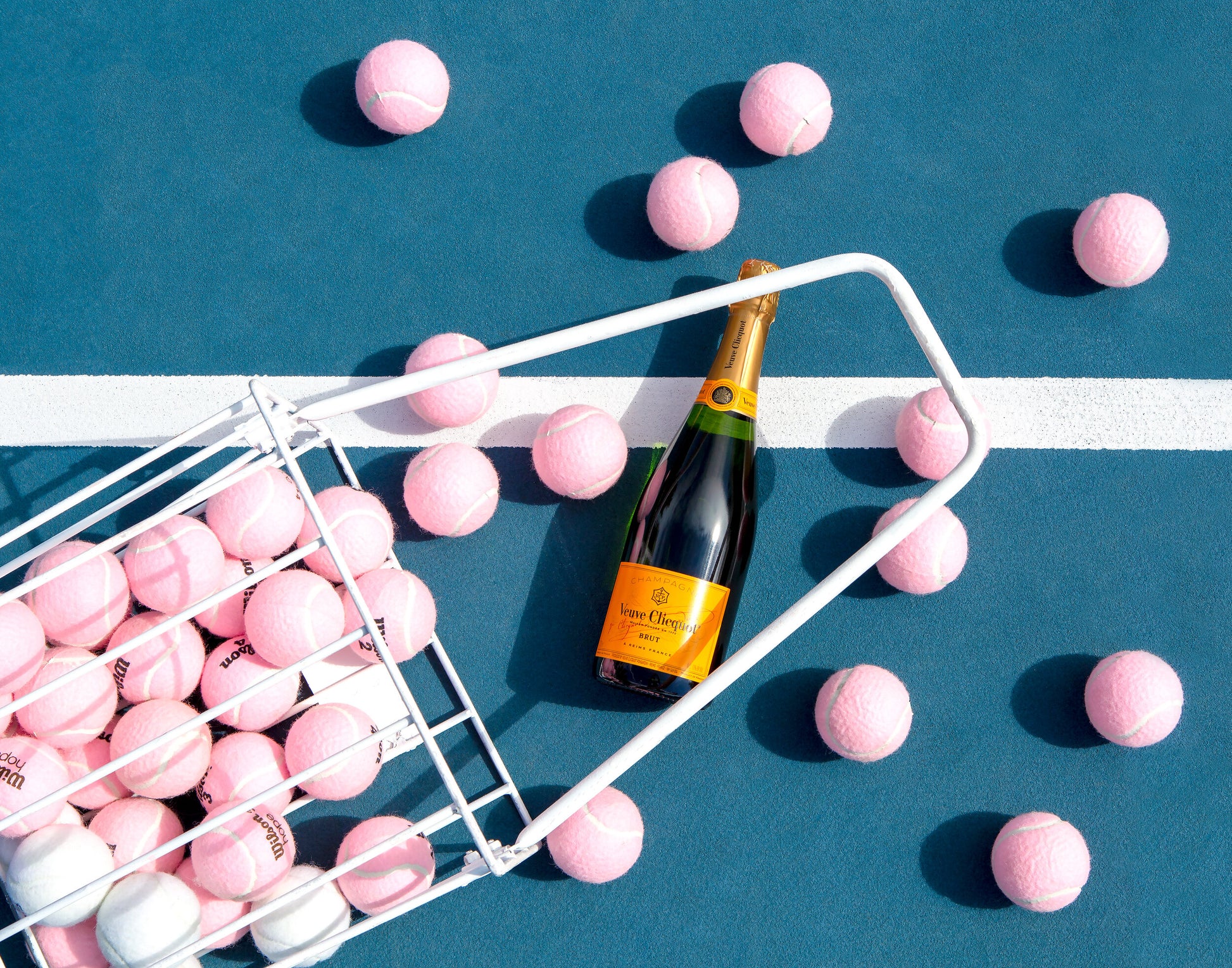 Pink tennis balls spilling out onto a blue tennis court around a bottle of Veuve Clicquot.