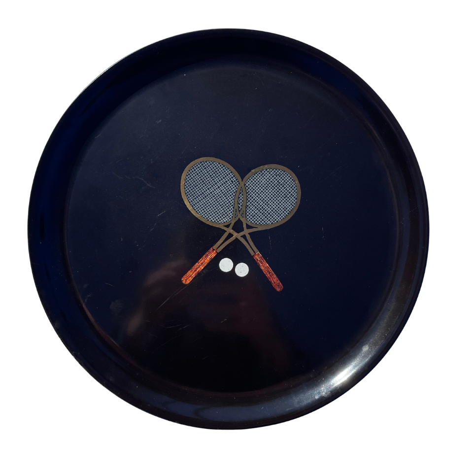 Black Couroc plate with two crossed tennis rackets and a ball on a white background