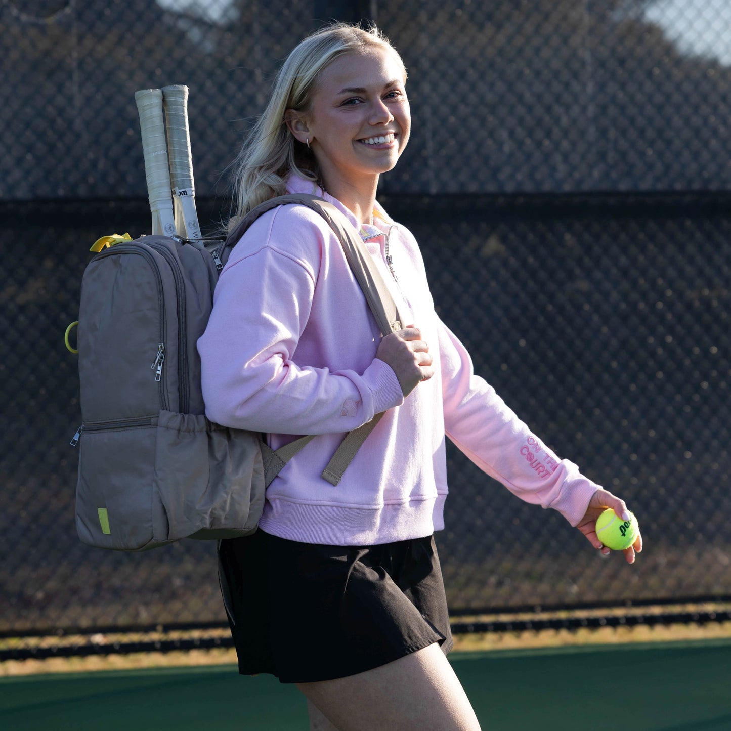 Woman on a tennis court with a backpack and tennis ball