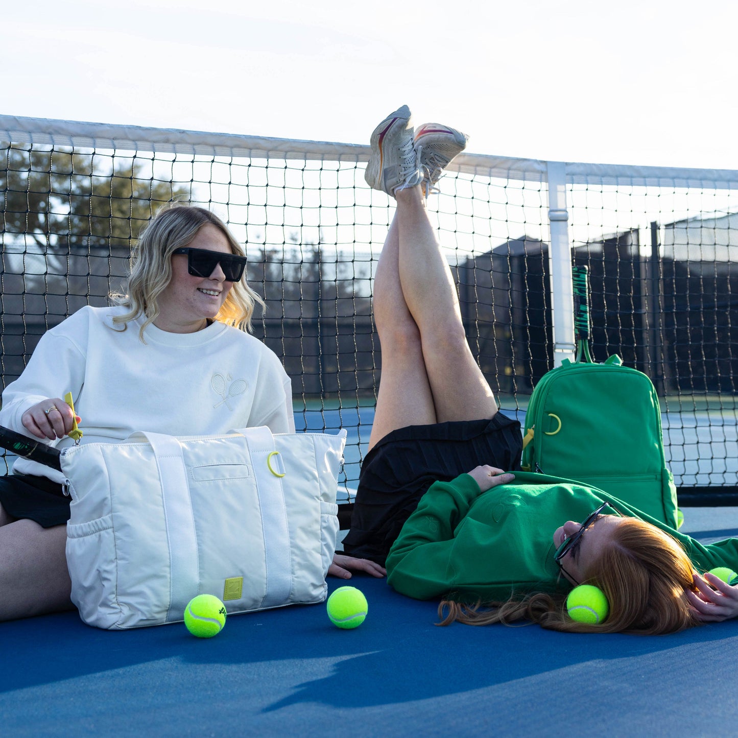 Two people lounging on a tennis court with sports equipment