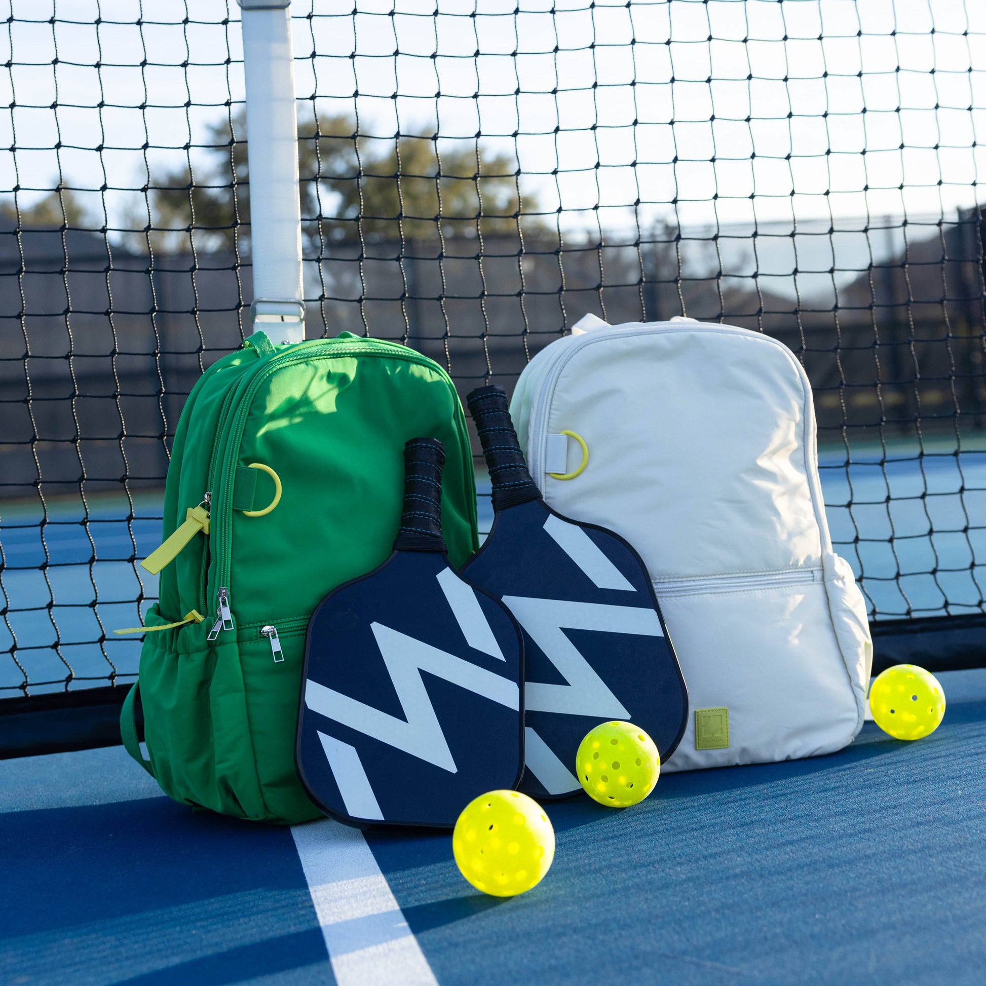 Two pickleball paddles with green and white bags on a tennis court