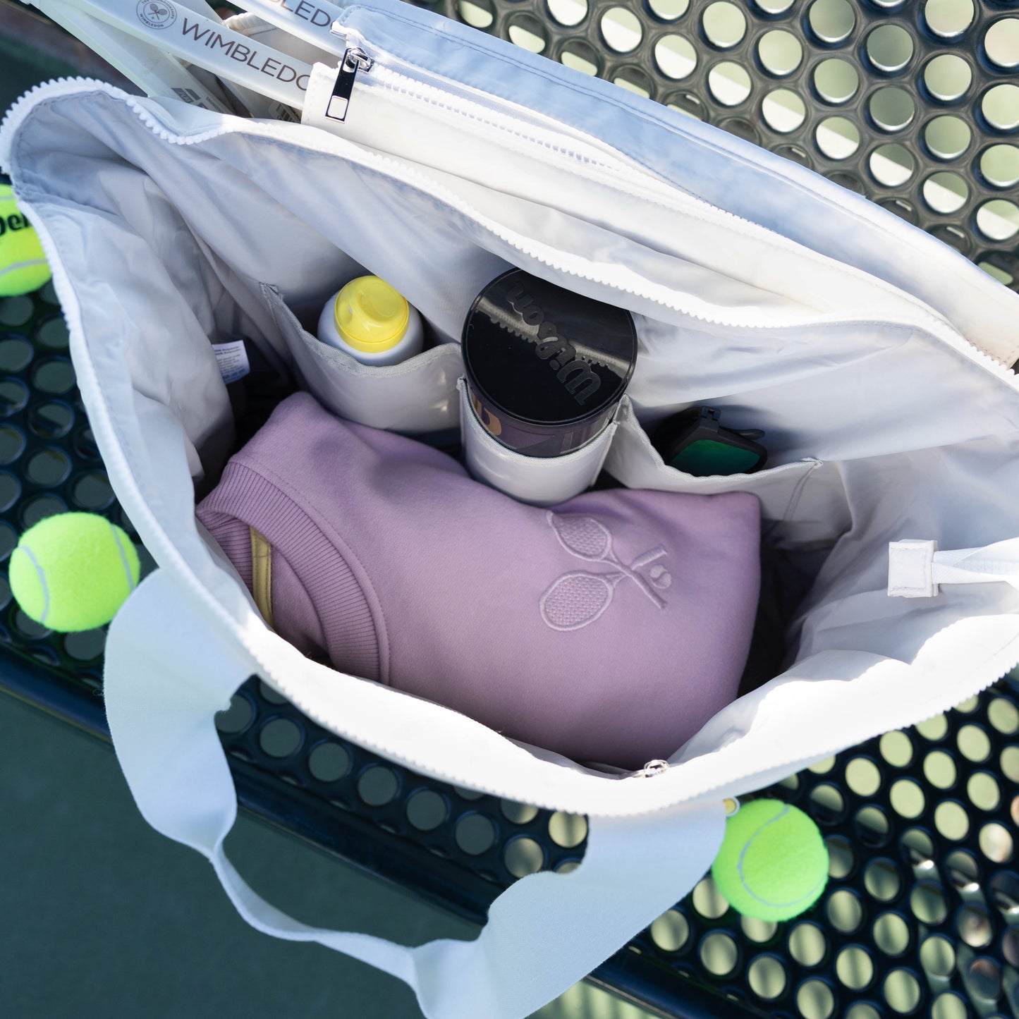 Open white bag with tennis balls and a purple item on a tennis court background