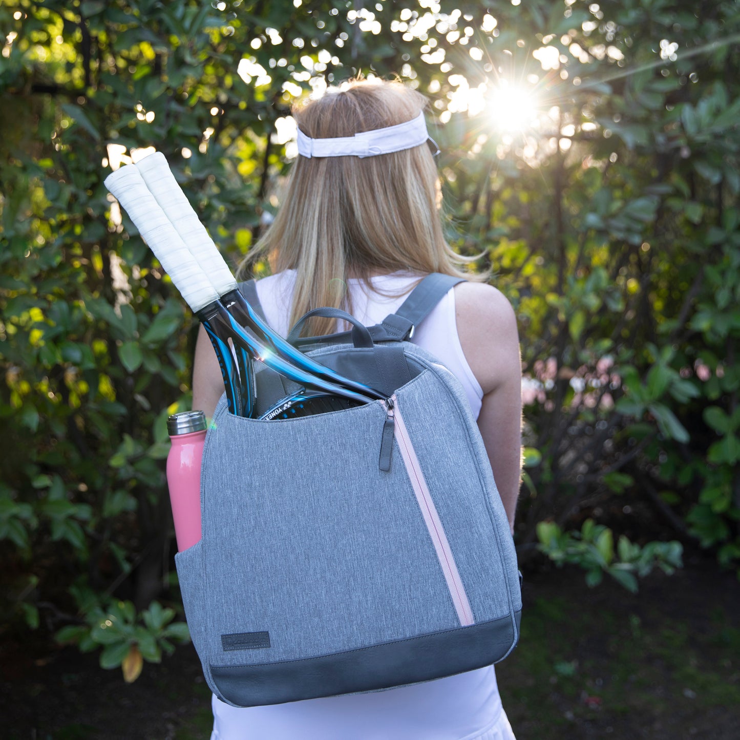 Person with a gray  Doubletake tennis backpack carrying tennis equipment outdoors
