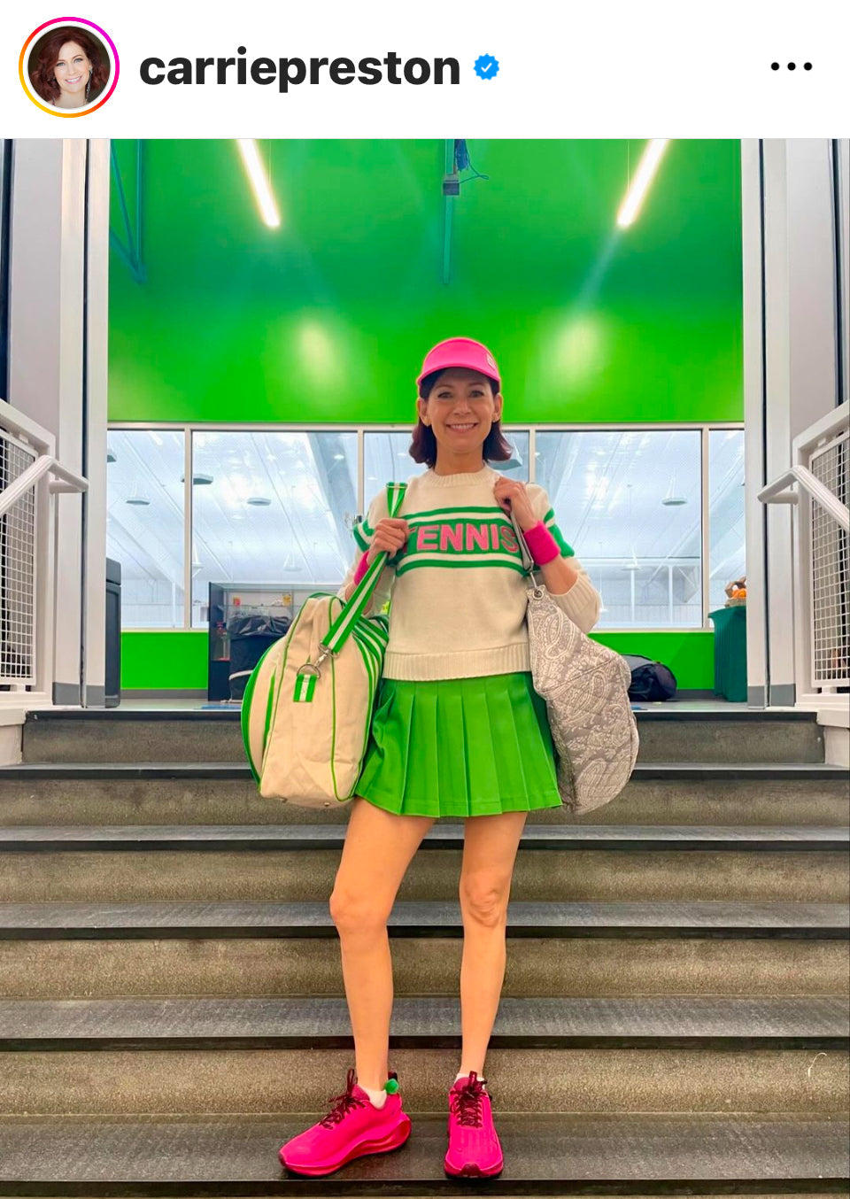 Person in tennis attire with a green background, holding sports bags.