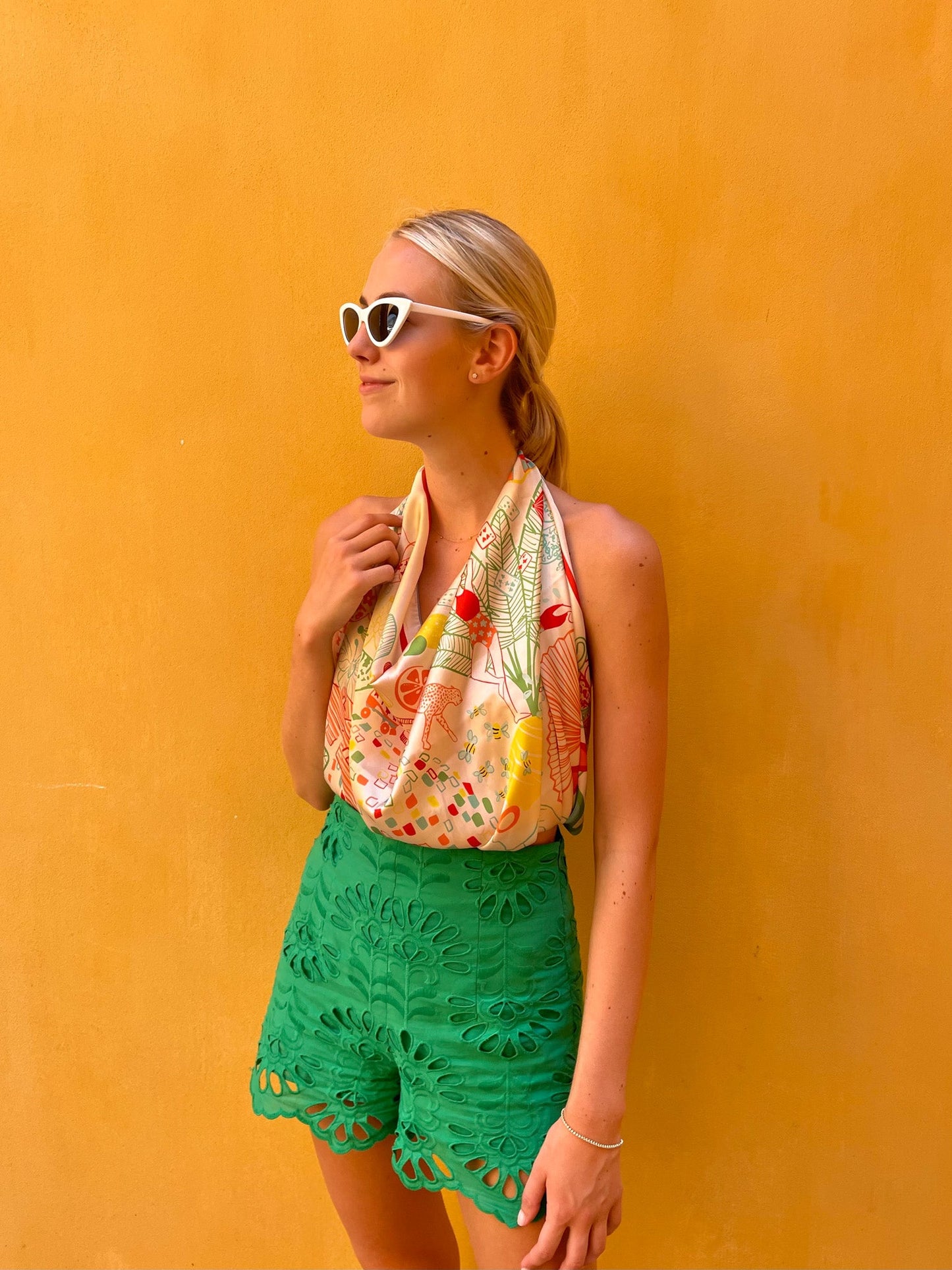 Woman wearing a colorful top and green shorts against an orange wall