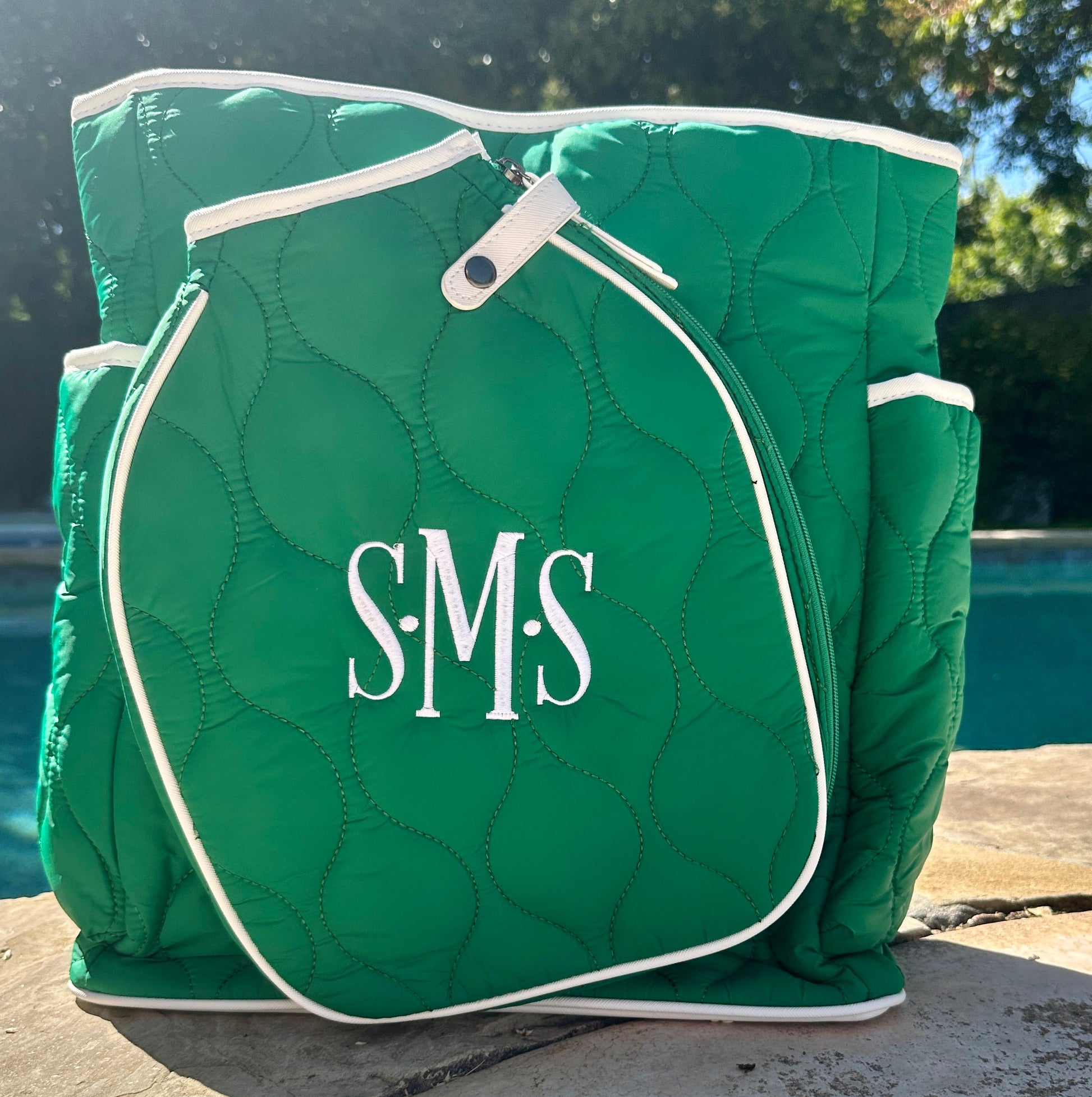 Green quilted bag with 'S.M.S' monogram on a poolside background