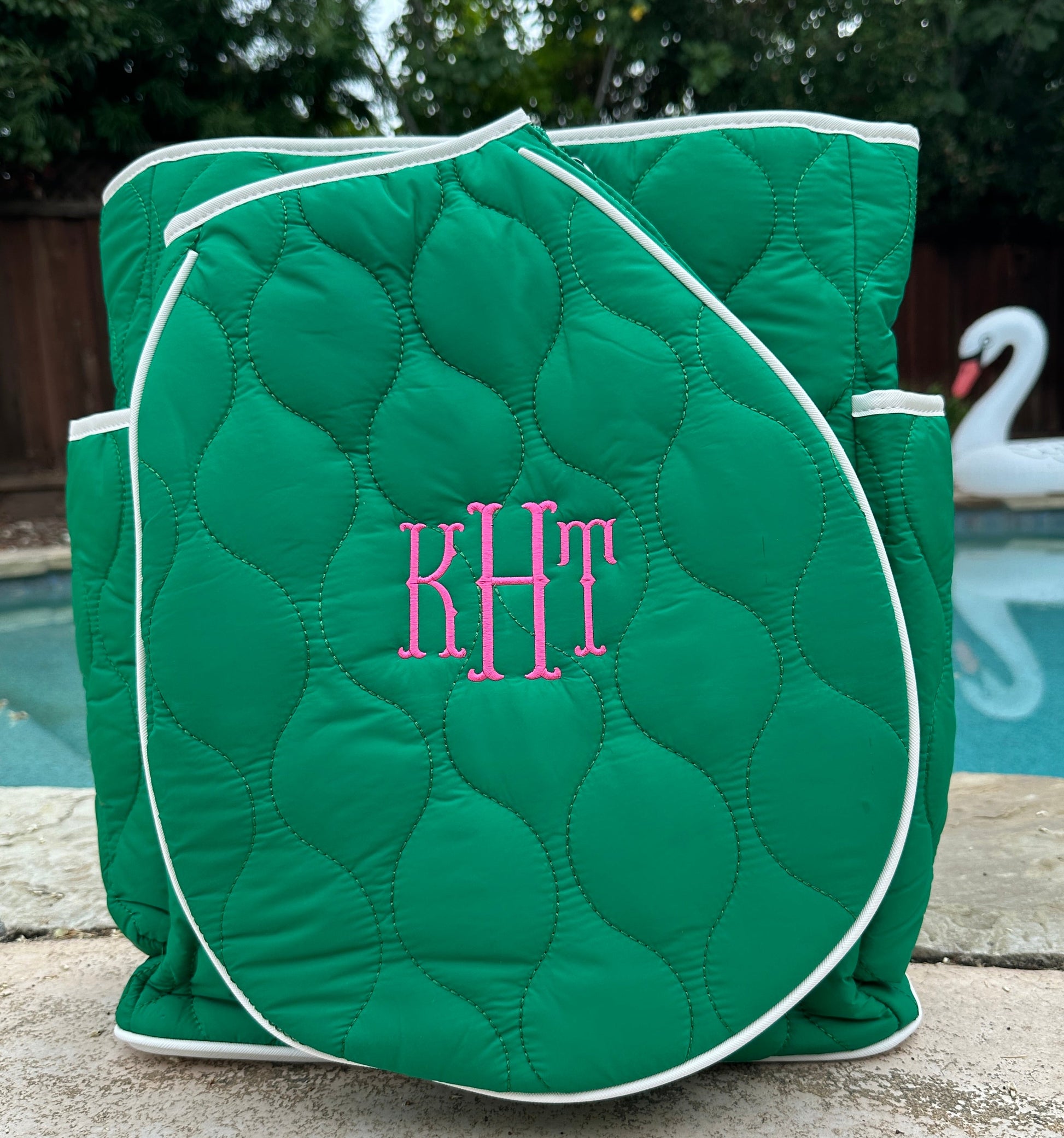 Green quilted tennis cover with pink monogram 'KHT' against a poolside background