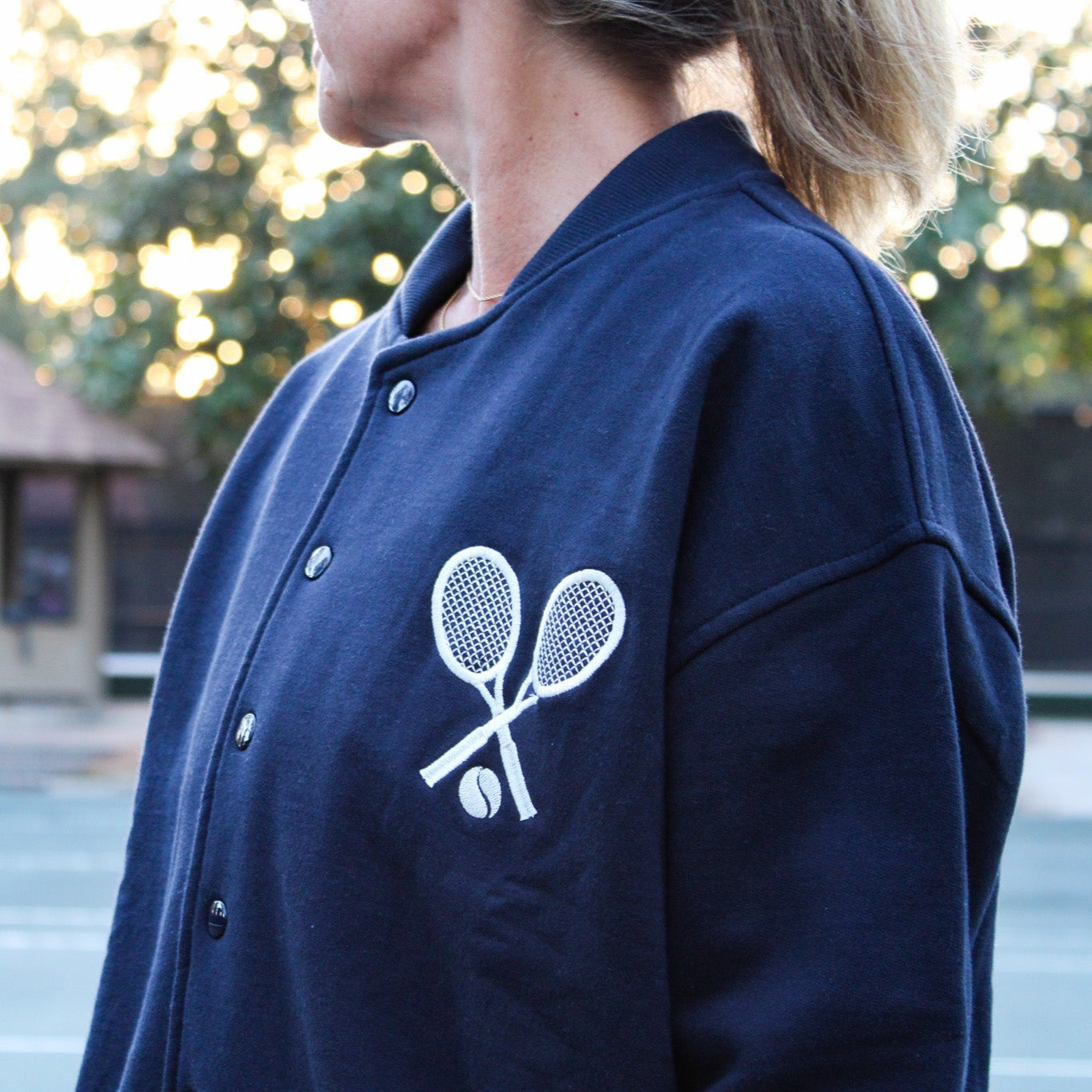 Navy blue jacket with tennis racket and ball design on a blurred outdoor background