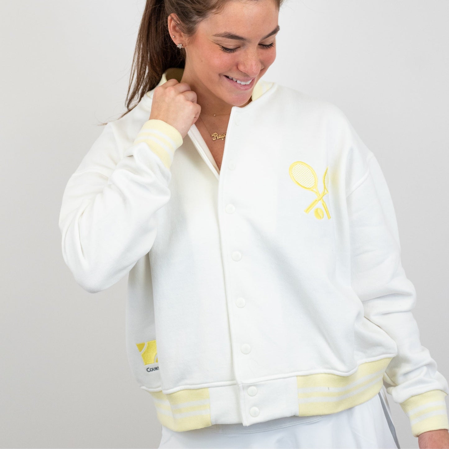 Woman wearing a white jacket with yellow accents and a logo on a plain background