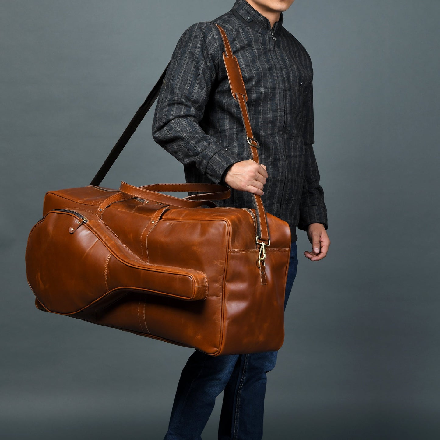 Person holding a brown leather duffel bag against a gray background
