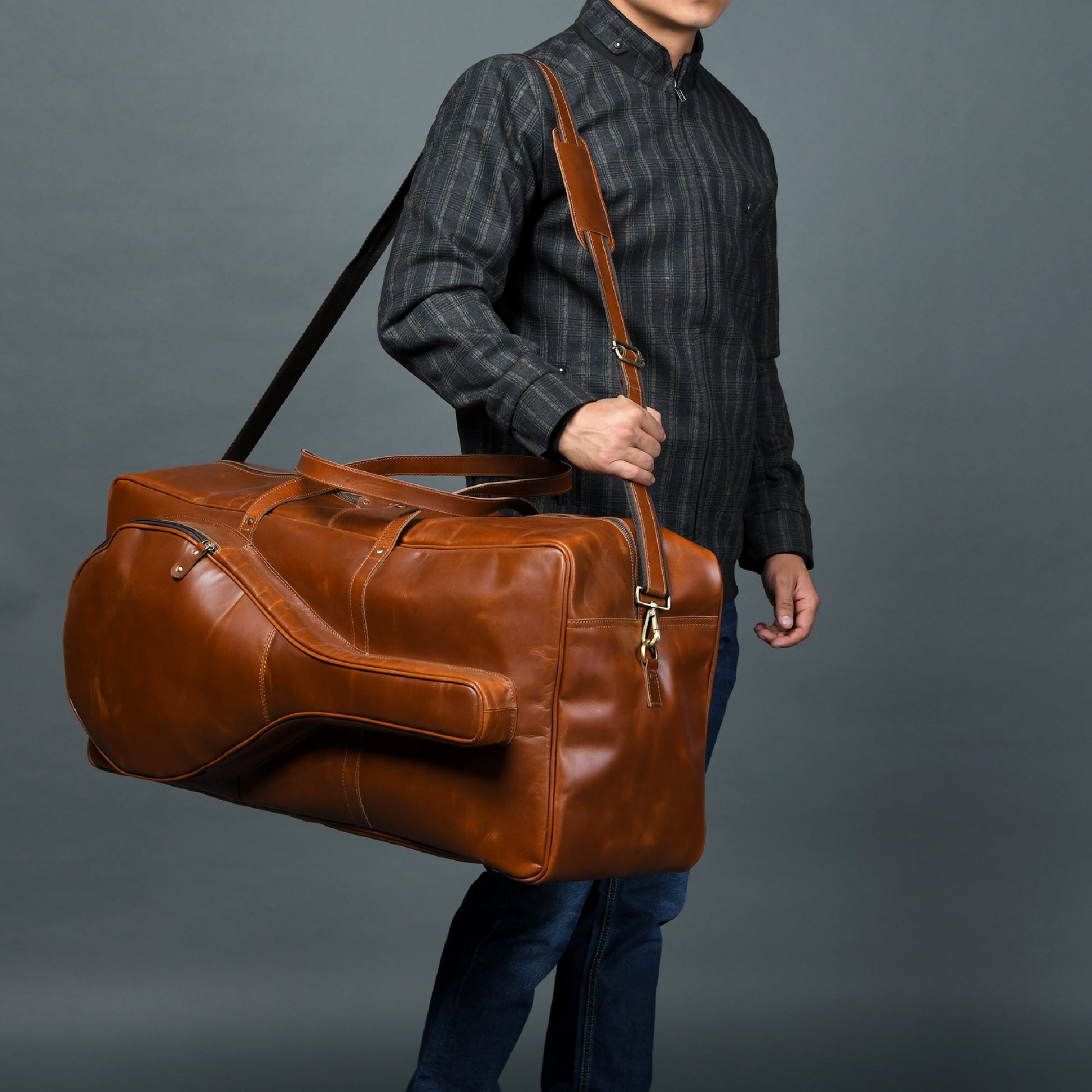 Person holding a brown leather duffel bag against a gray background