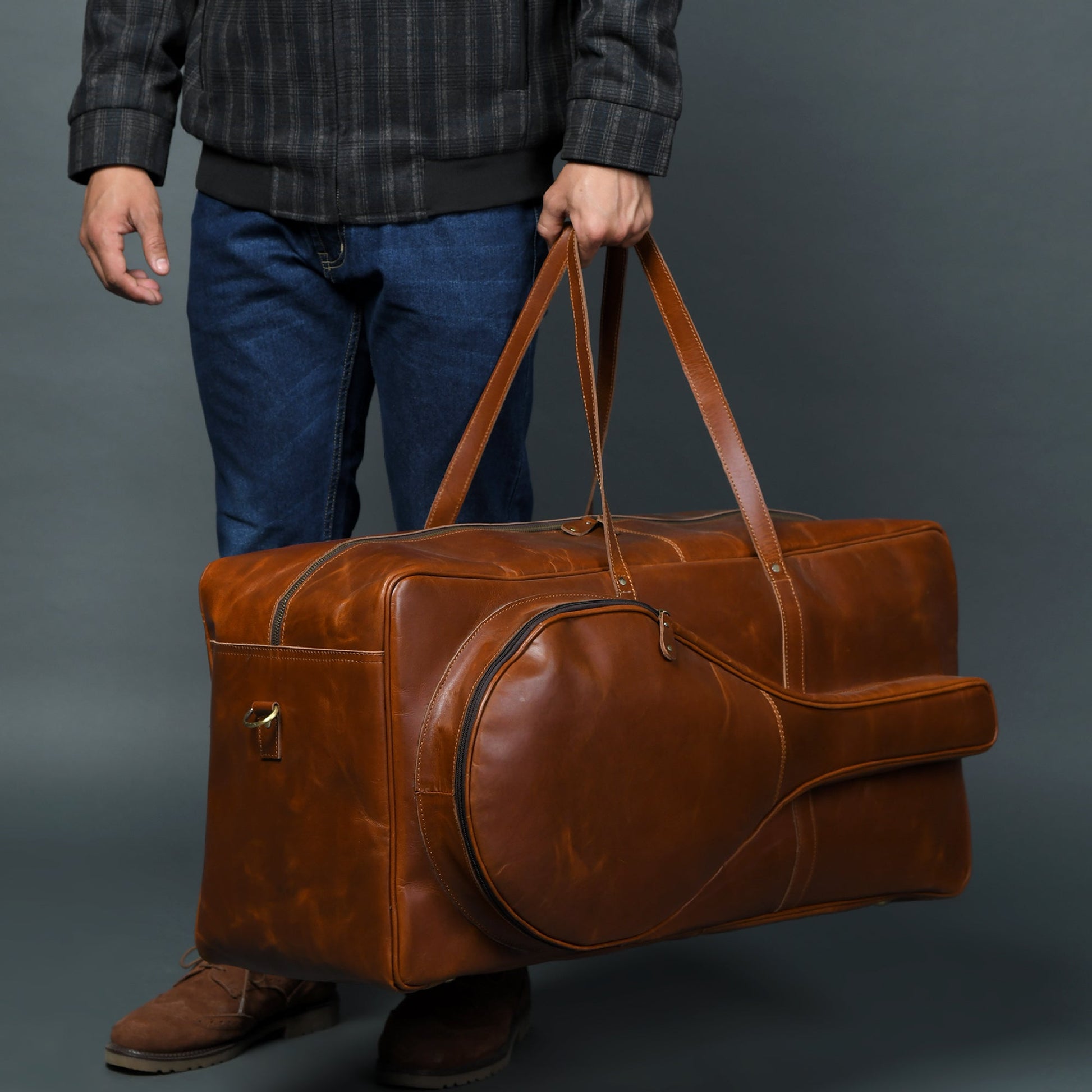 Person holding a brown leather duffel bag against a gray background