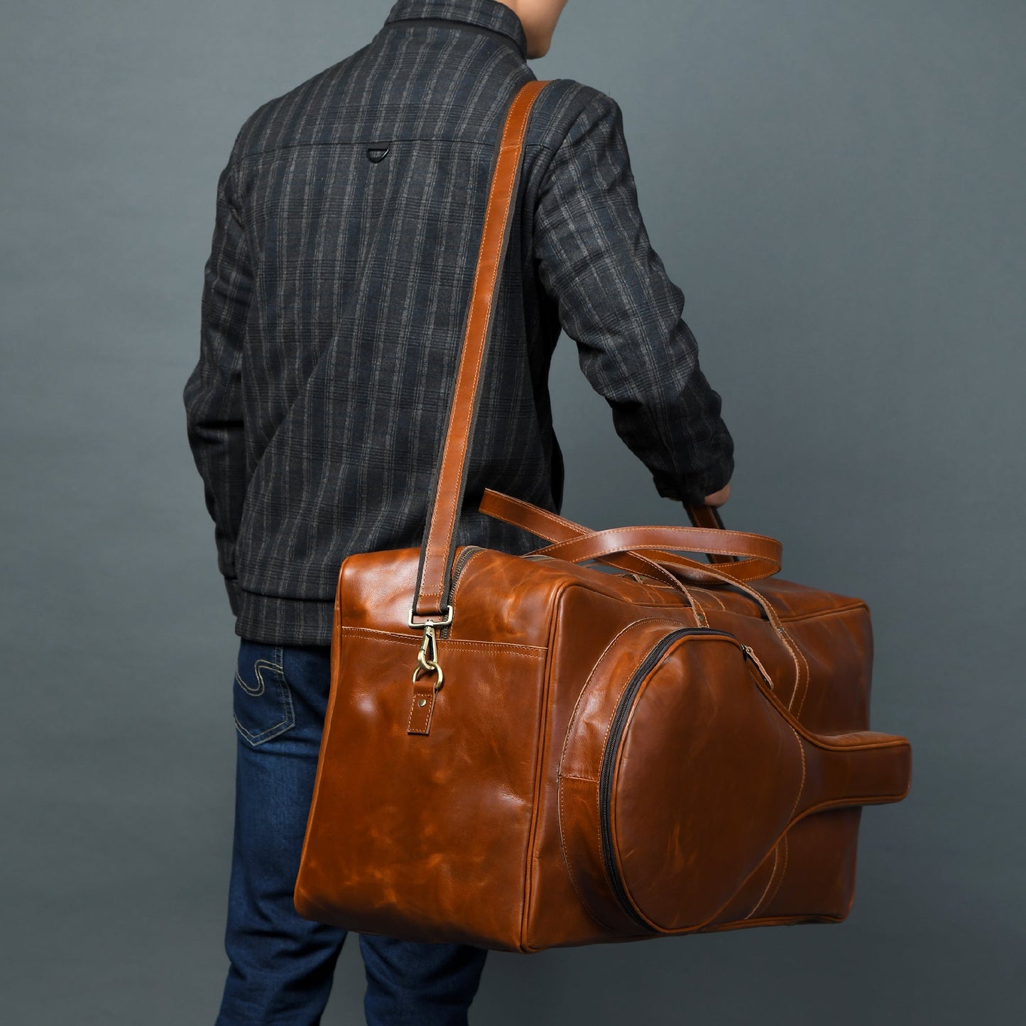 Person holding a brown leather duffel bag against a gray background