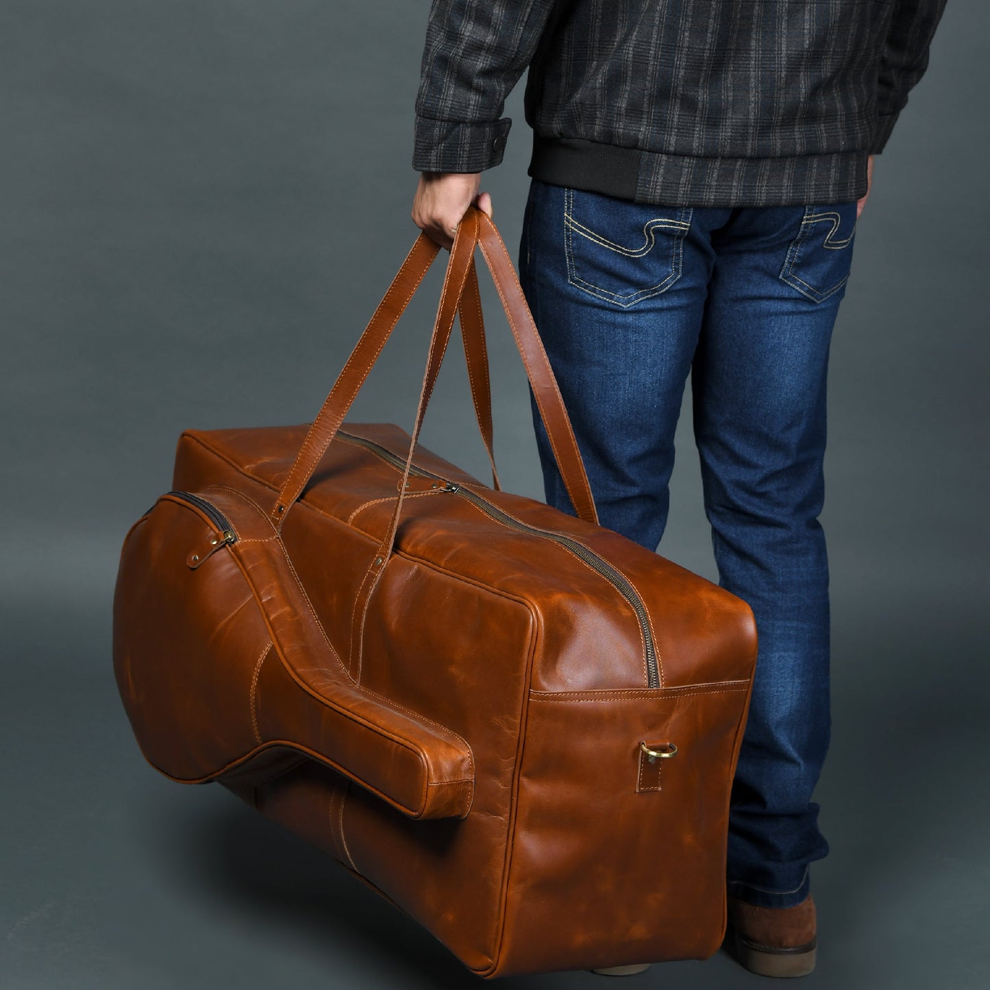 Person holding a brown leather duffel bag against a gray background