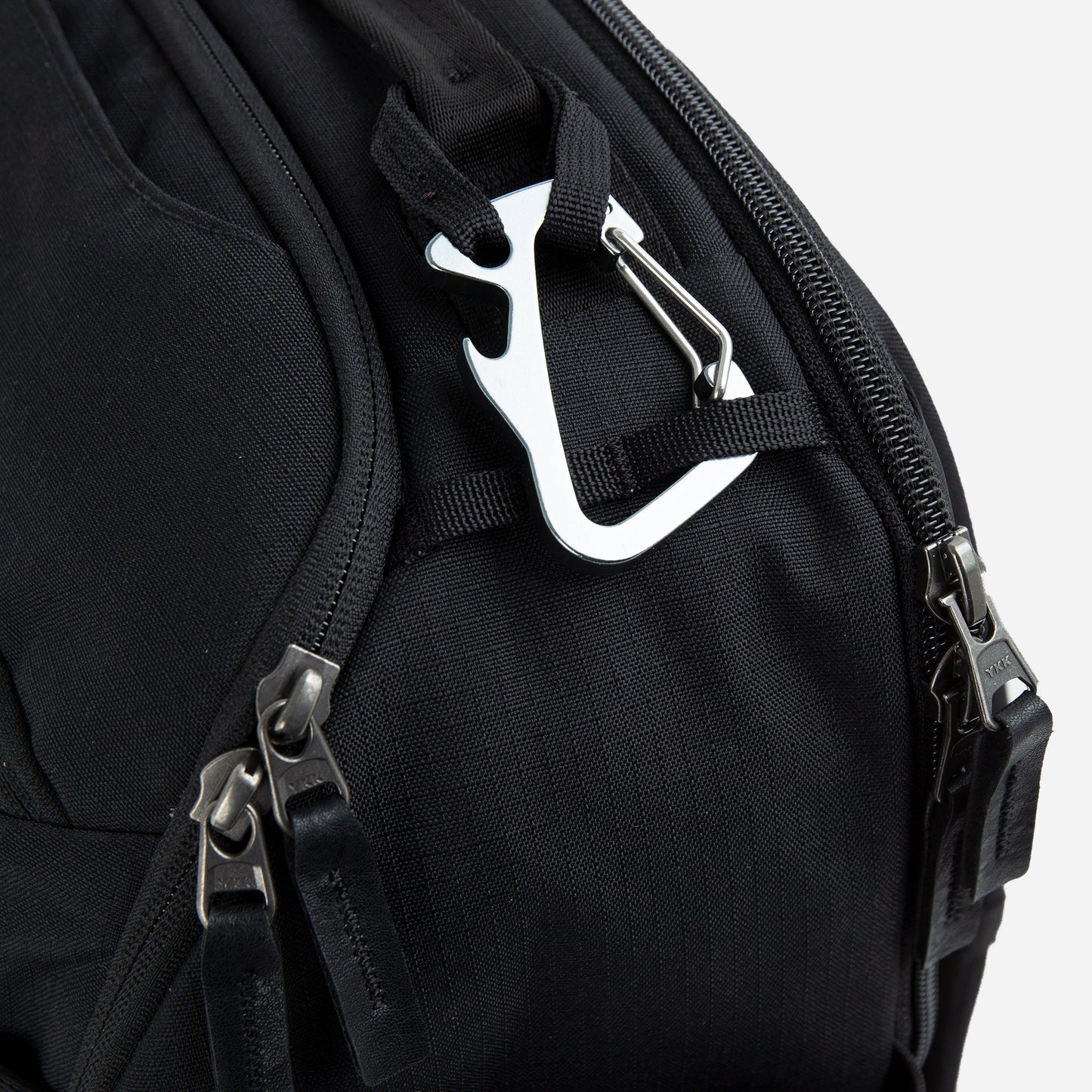 Close-up of a black Doubletake tennis backpack with metal carabiner and zippers on a white background