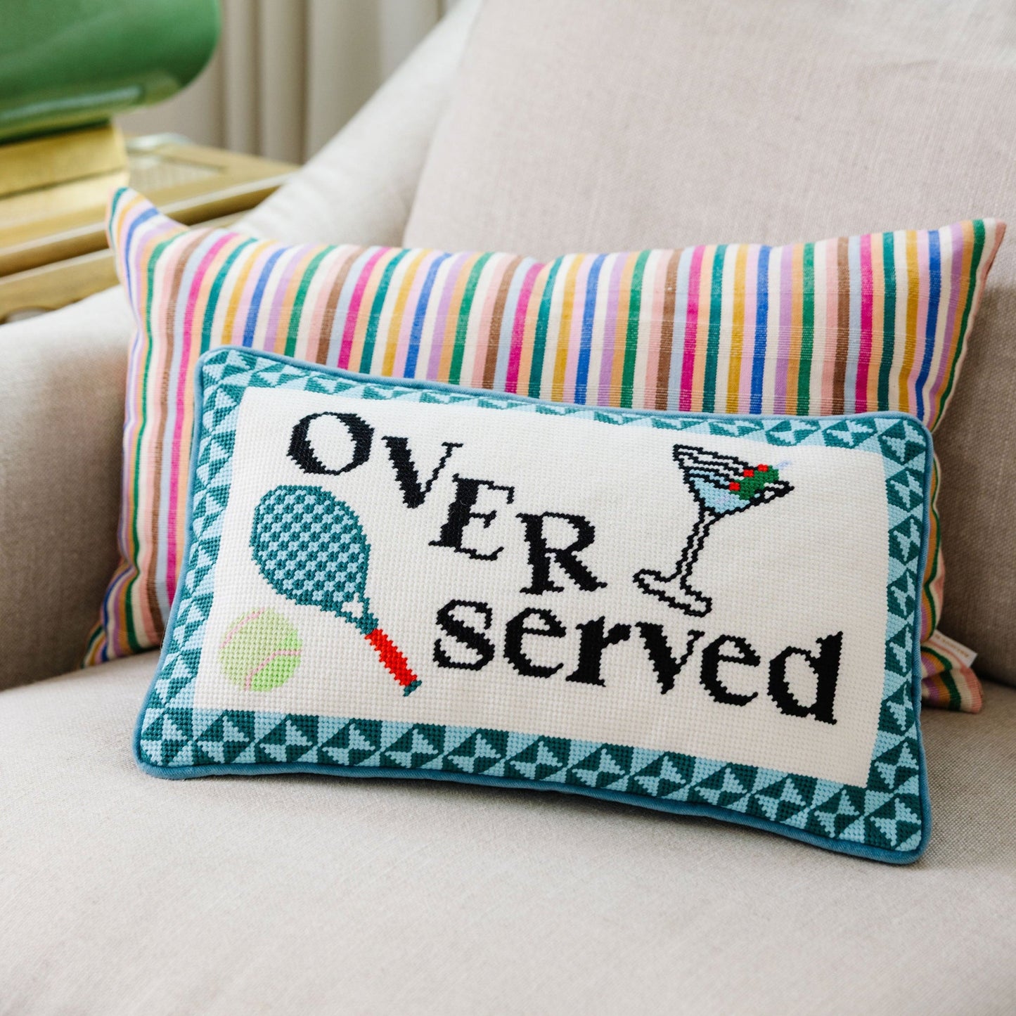 Decorative pillow with 'Over served' text and tennis racket design on a couch.