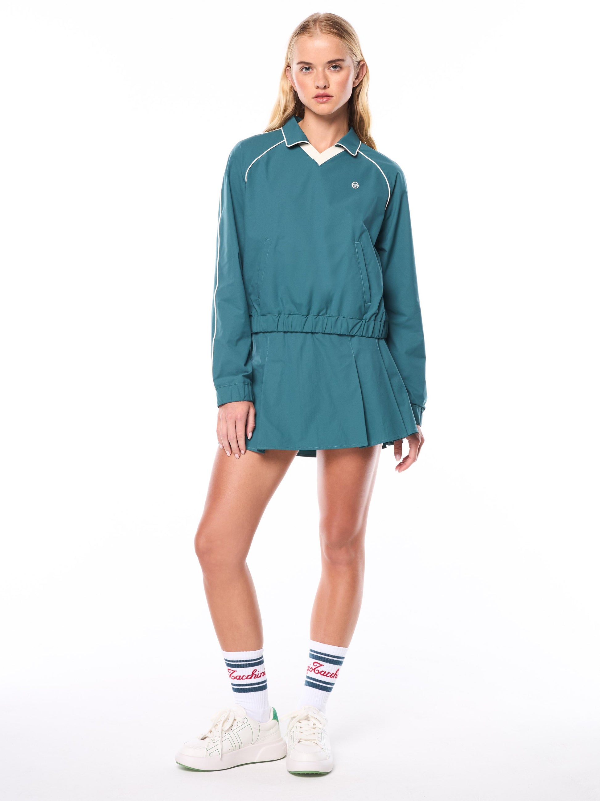 Woman wearing a teal tracksuit with white sneakers on a white background