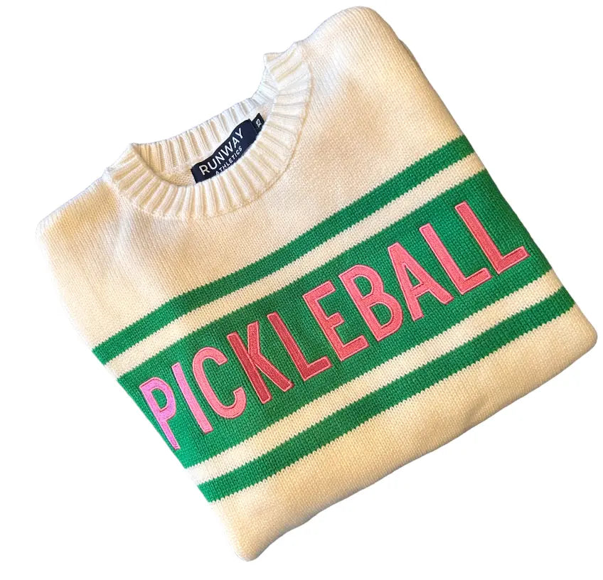 Folded beige sweater with 'Pickleball' text in pink on a green stripe, brand 'Runway' visible.