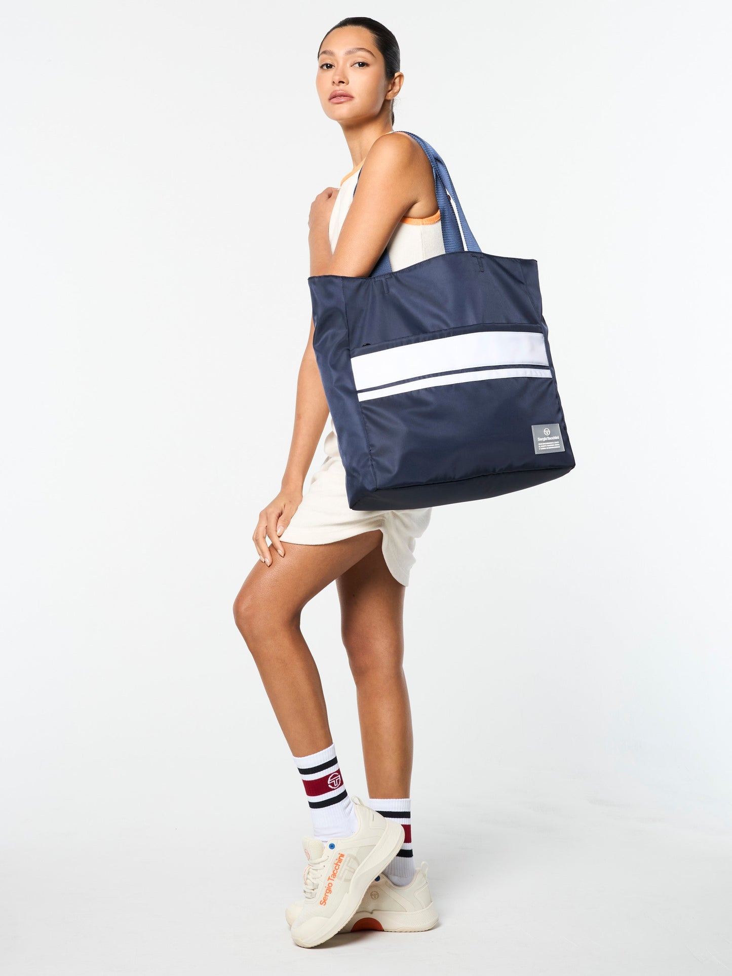 Woman holding a navy tote bag with a white stripe on a white background