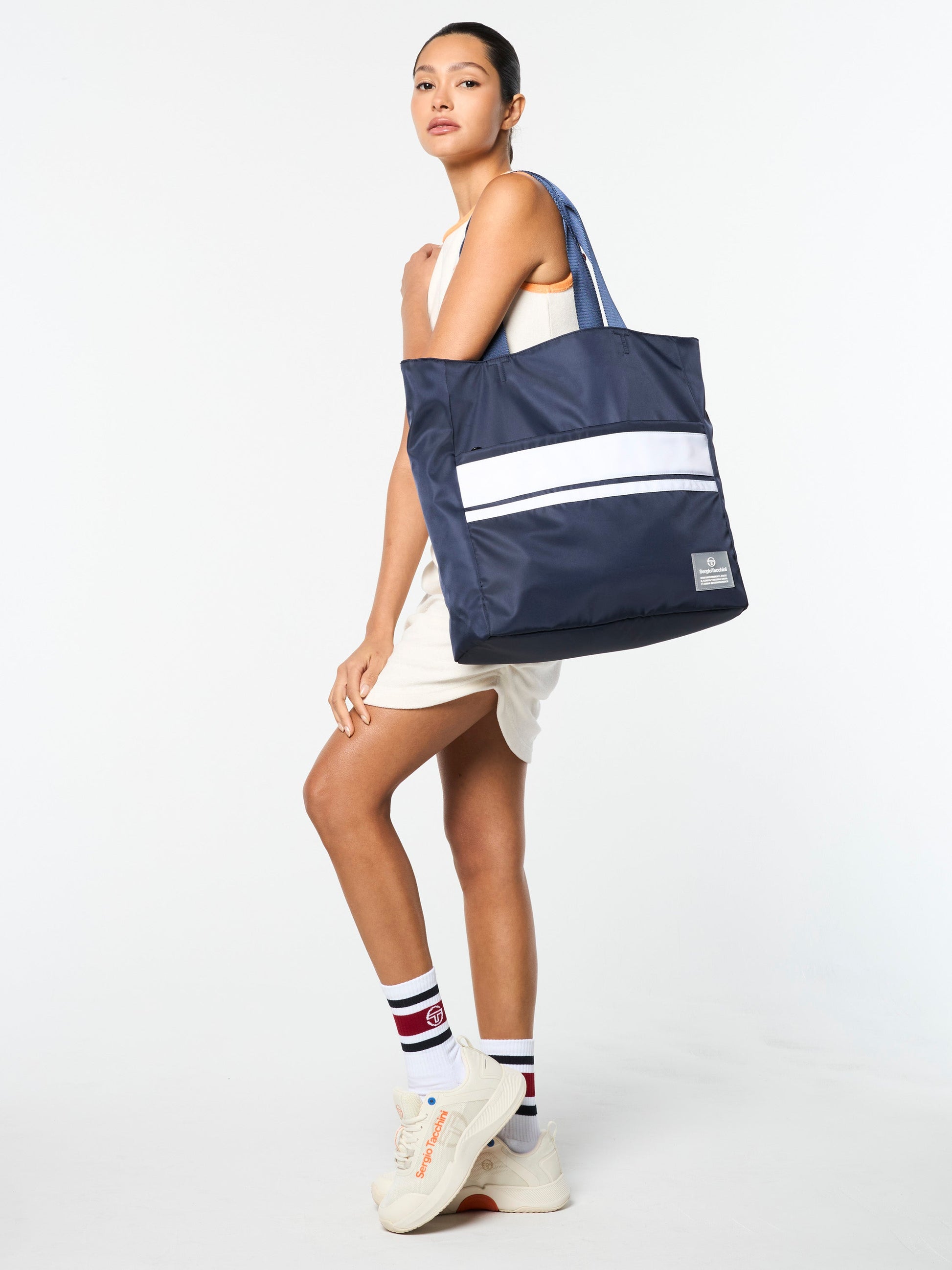 Woman holding a navy tote bag with a white stripe on a white background