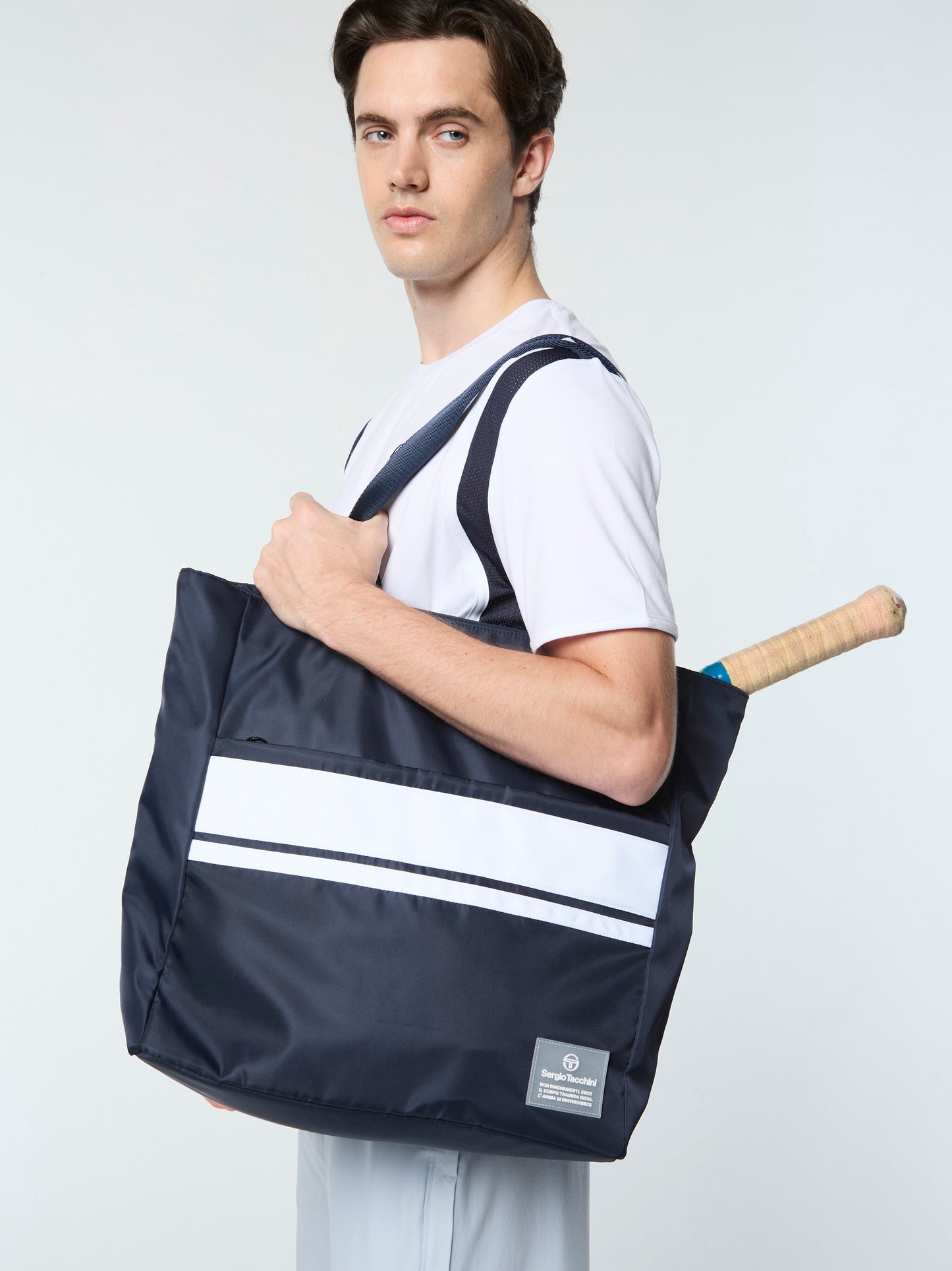 Person holding a navy blue bag with white stripes against a light gray background