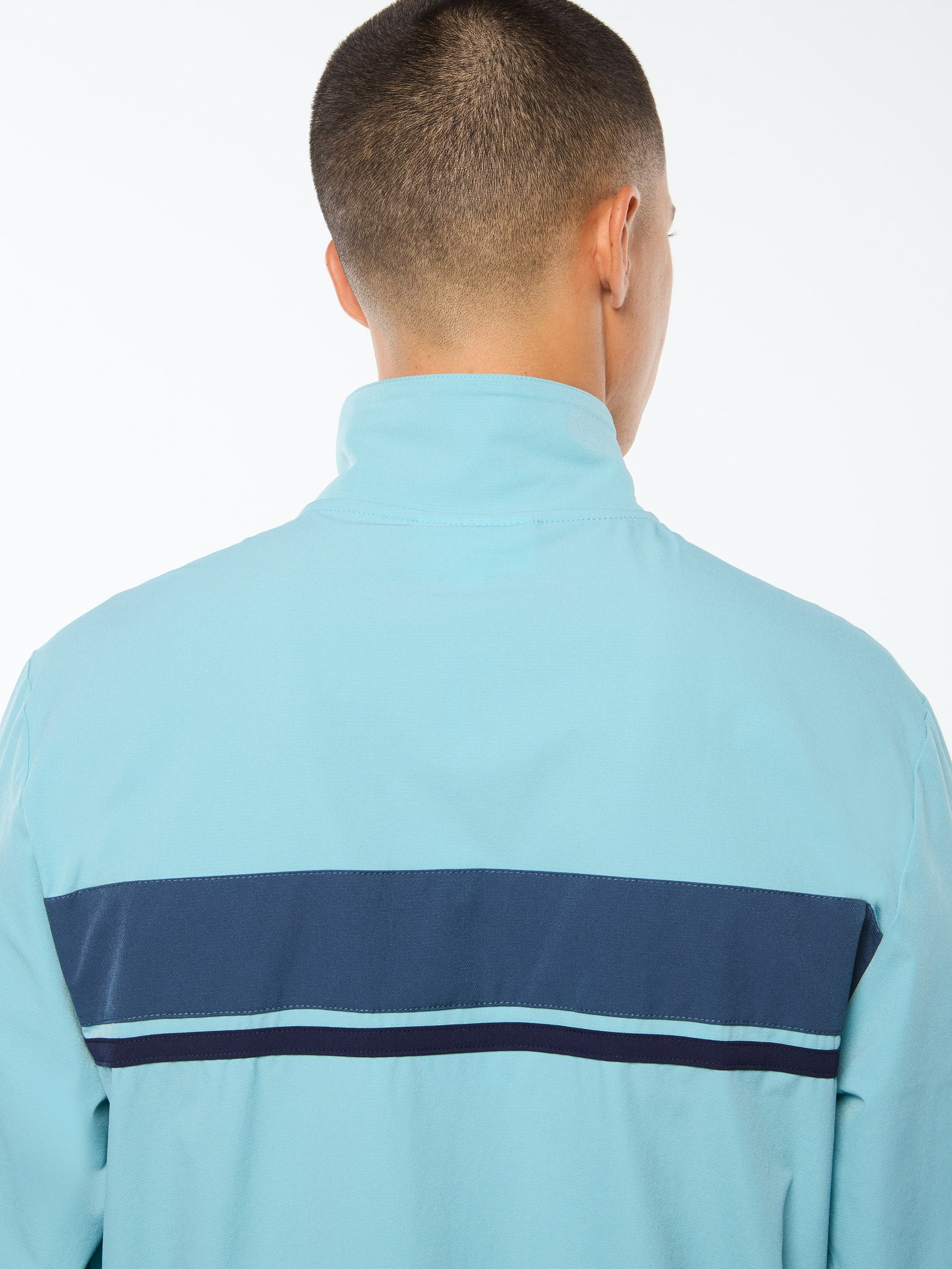 Person wearing a light blue jacket with a dark blue stripe on the back against a white background