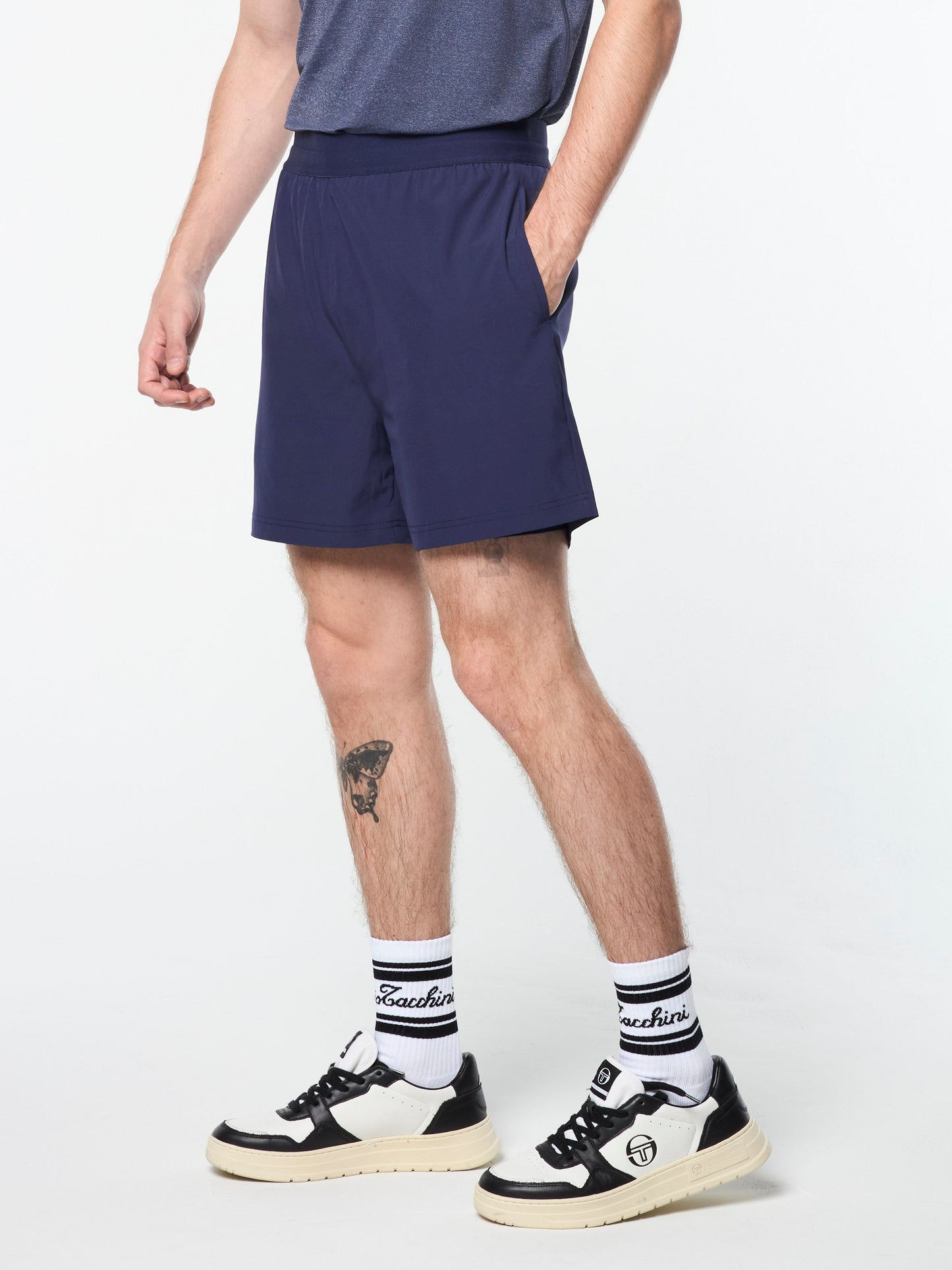 Person wearing navy shorts, black and white sneakers, and socks with a brand logo on a white background
