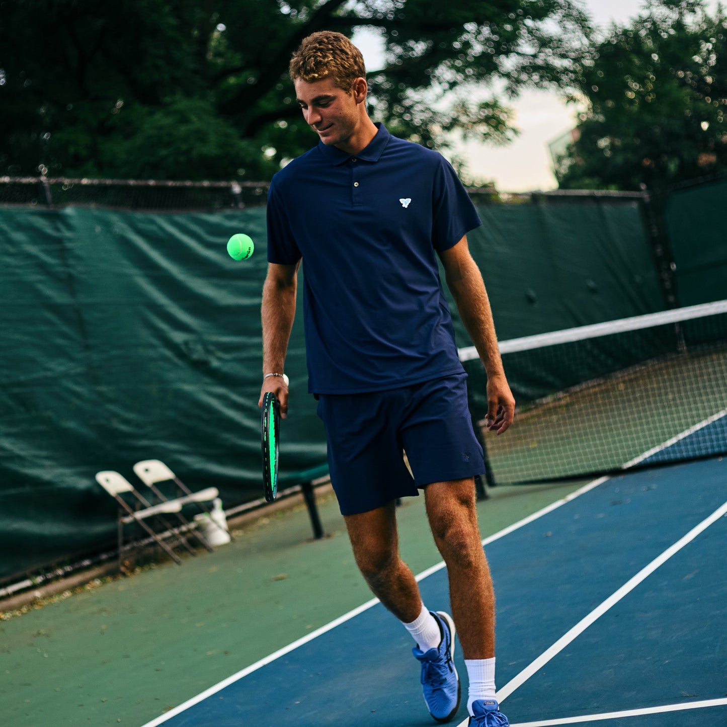 Man on a tennis court holding a racket and ball, wearing a navy blue outfit.