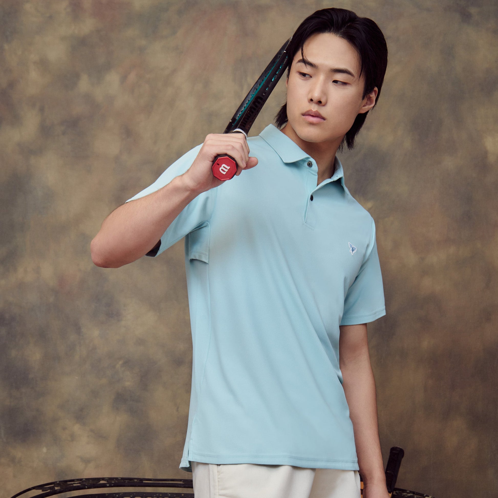 Person wearing a light blue polo shirt holding a baseball bat against a textured brown background