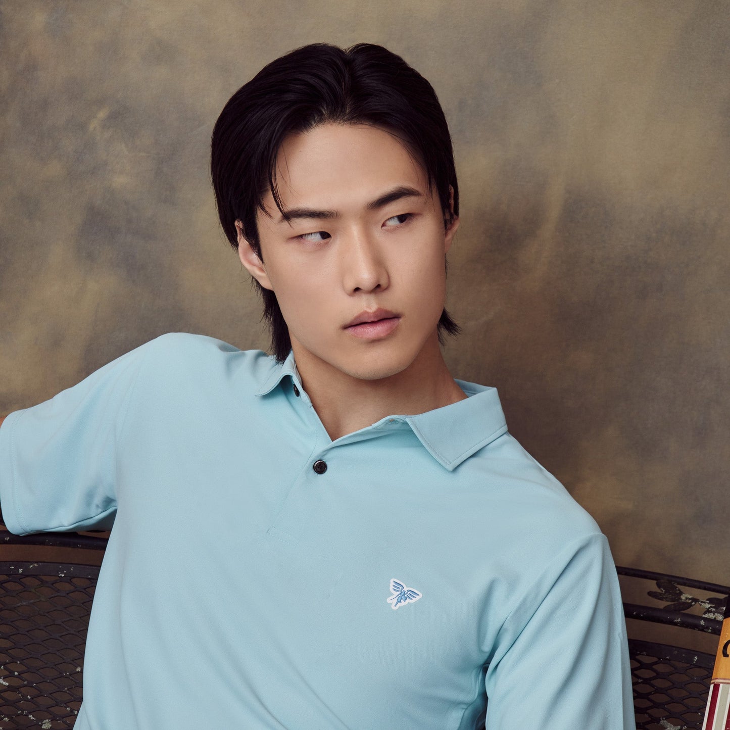 Man wearing a light blue polo shirt with a logo against a textured brown background