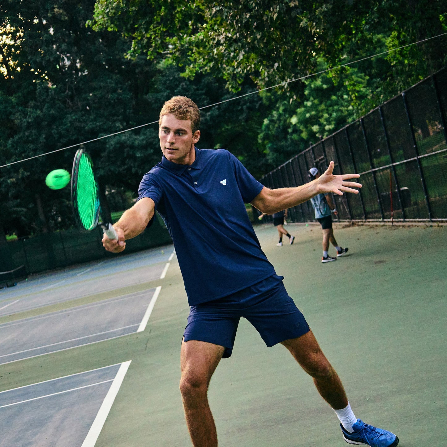 Man playing pickleball on an outdoor court with trees in the background